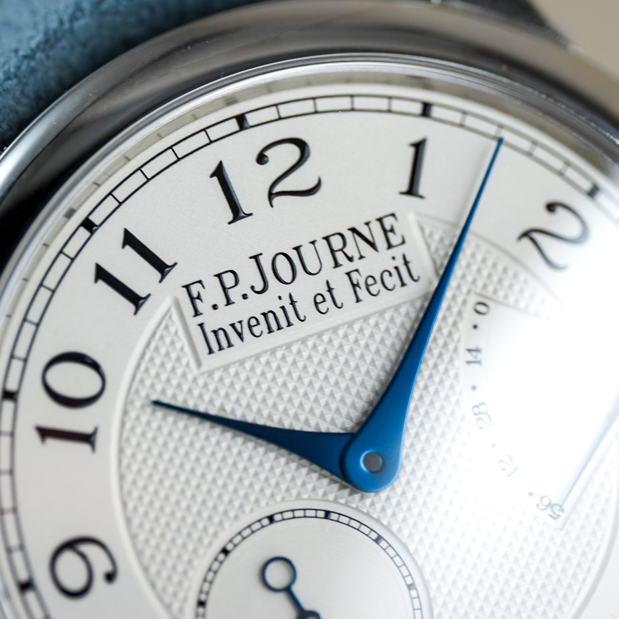 Closeup of a F.P.Journe white watch dial with blue hands and a light blue strap. "Invenit et Fecit" is legible on the dial