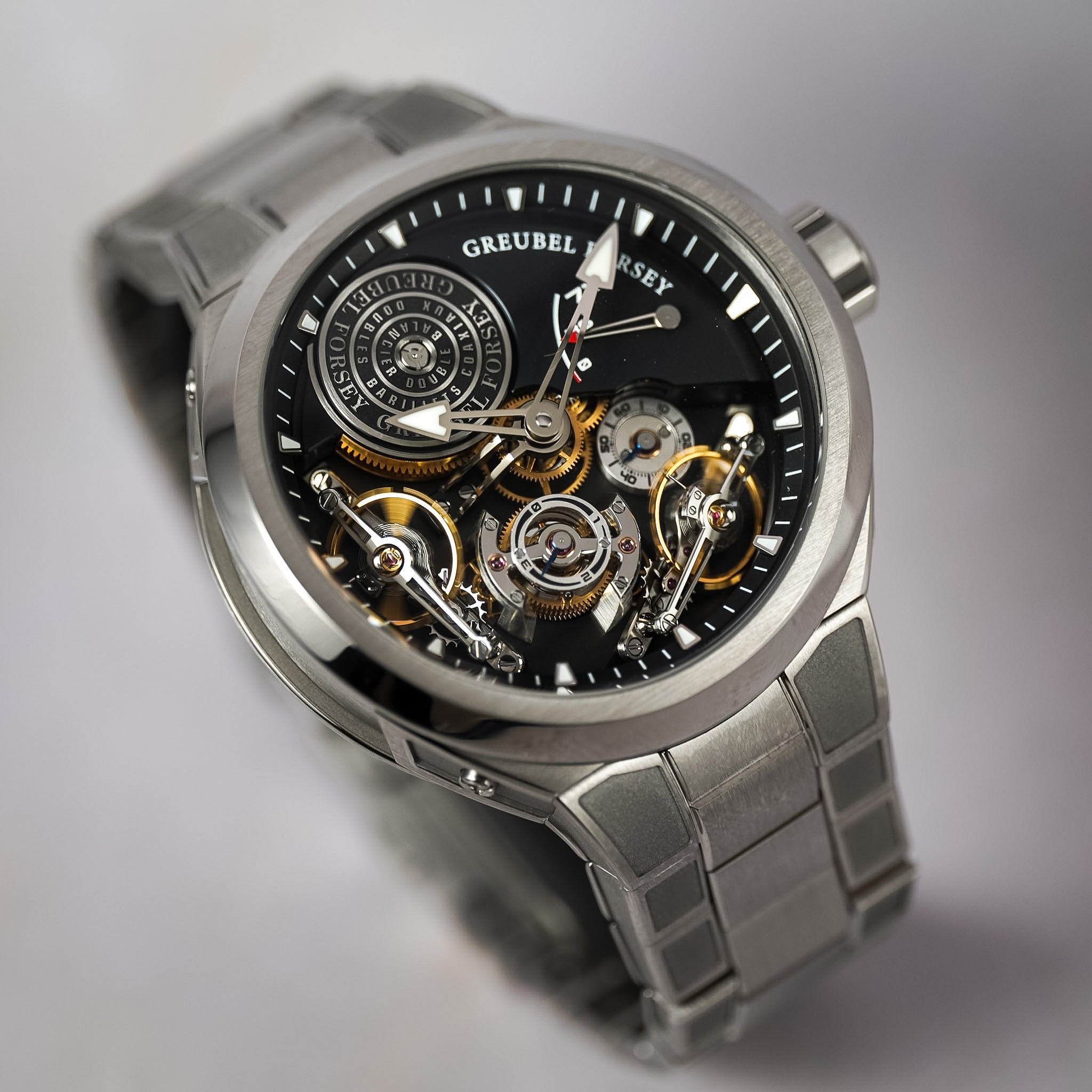 A Greubel Forsey wristwatch with a titanium case and link bracelet, featuring a black skeleton dial that reveals intricate gold and silver mechanical gears.