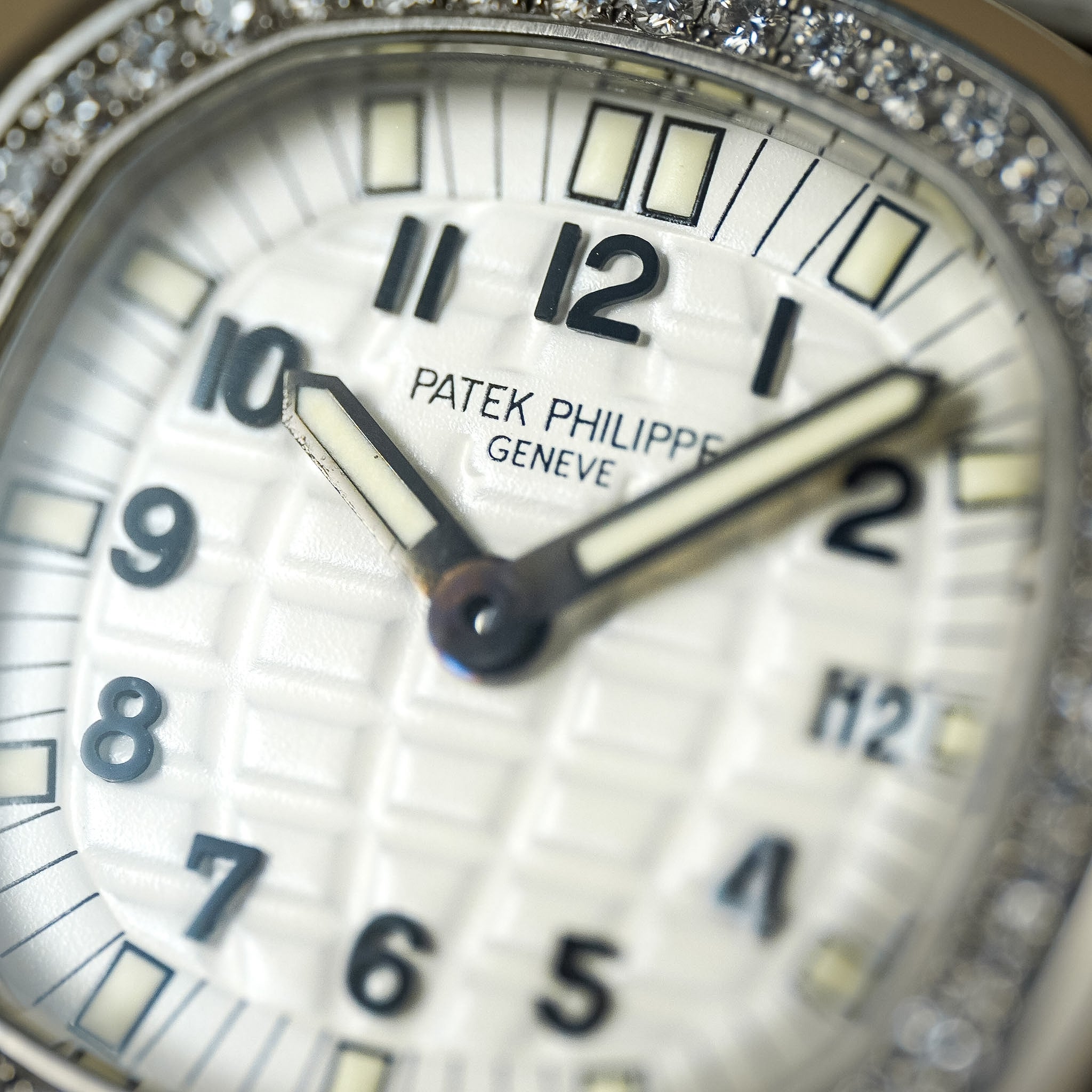 Closeup shot of a white dial Patek Philippe watch with a diamond bezel, black Arabic numeral hour markers, off-white hour markers, and a diamond bezel.