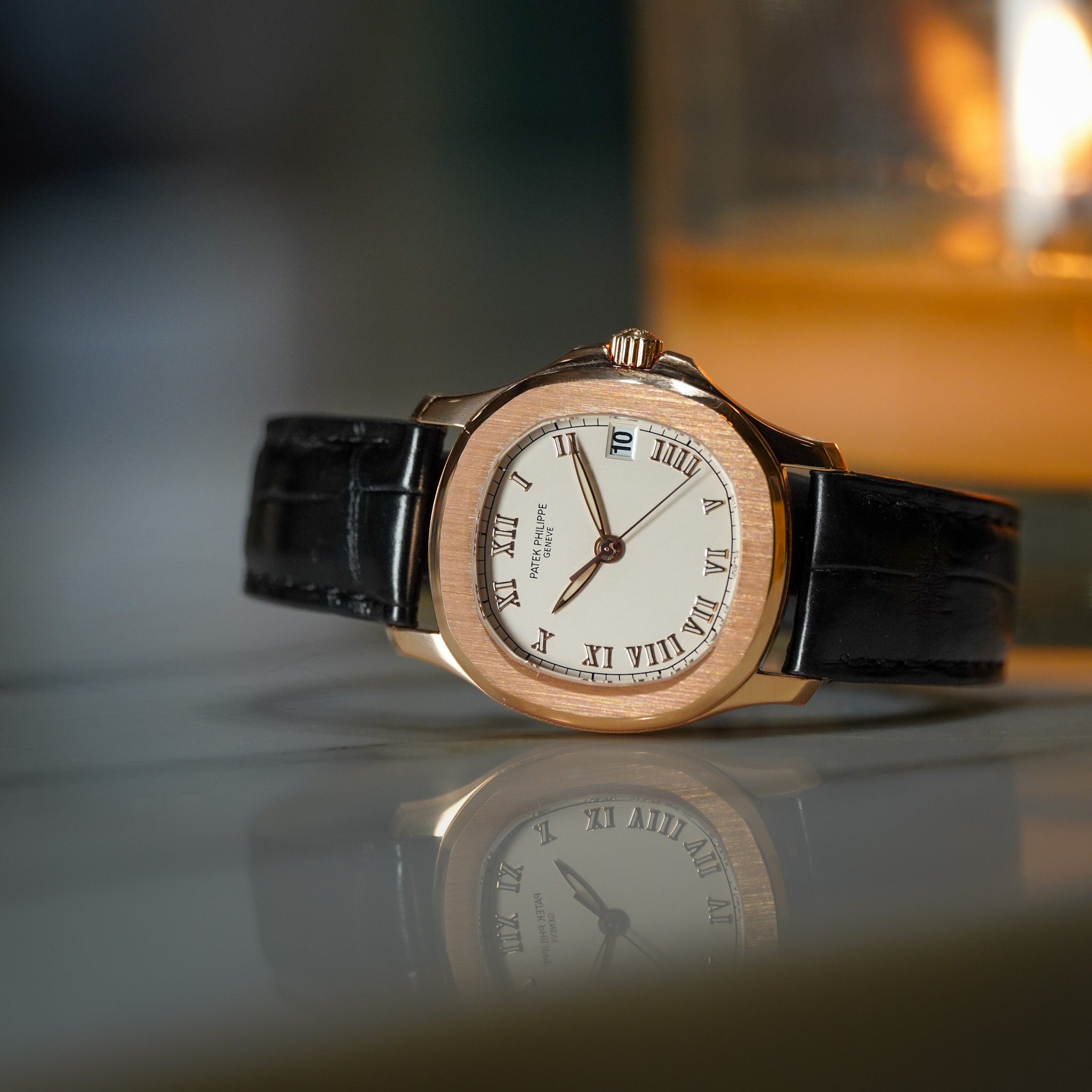 A Perpetual watch by Swatch, featuring a rose gold-tone wood-grain bezel, a white dial with black Roman numerals, and a black leather strap, resting on a reflective surface with a warm, blurred background.