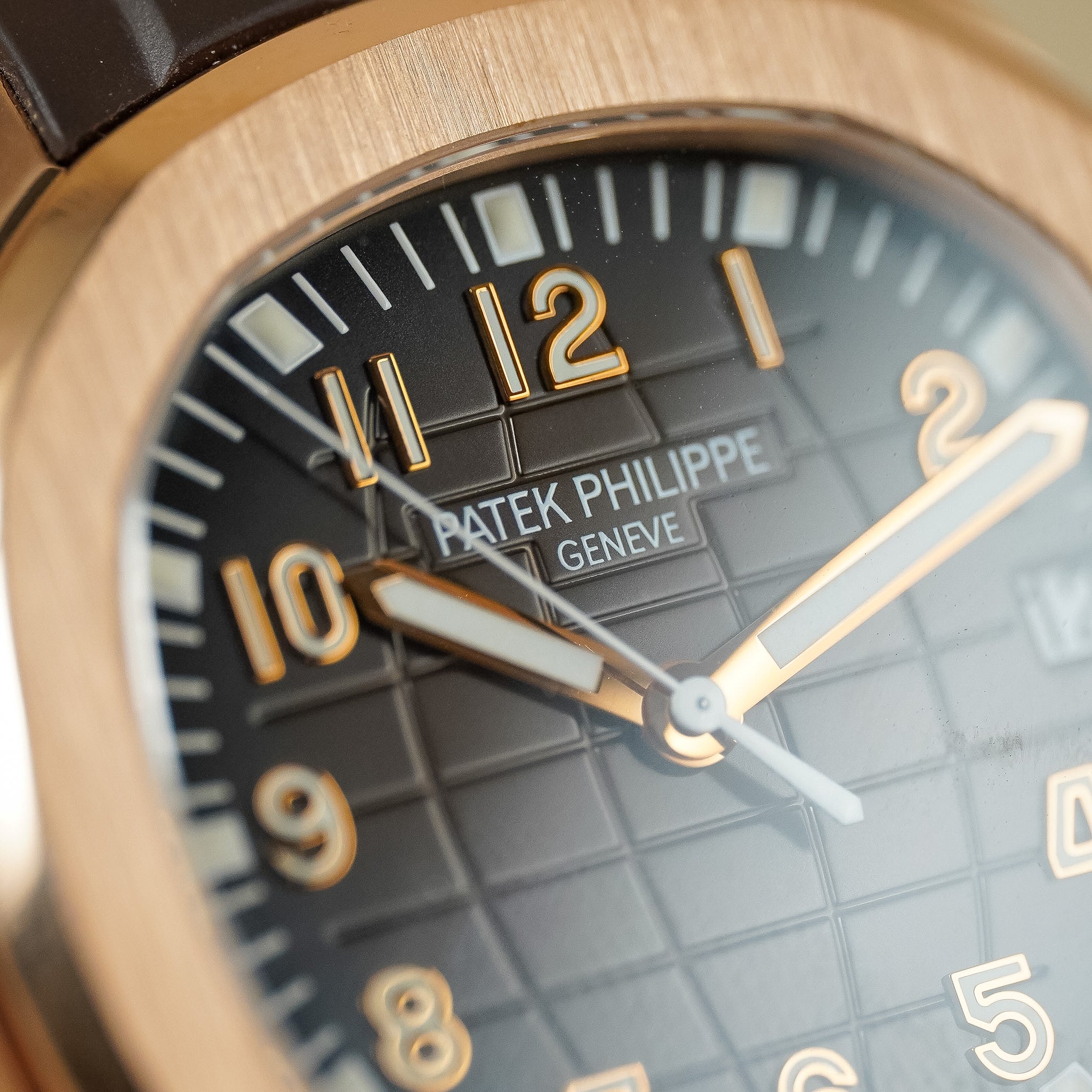 Closeup of a Patek Philippe watch with a rose gold case, hands, and hour markers. The watch features a textured, dark brown dial. 