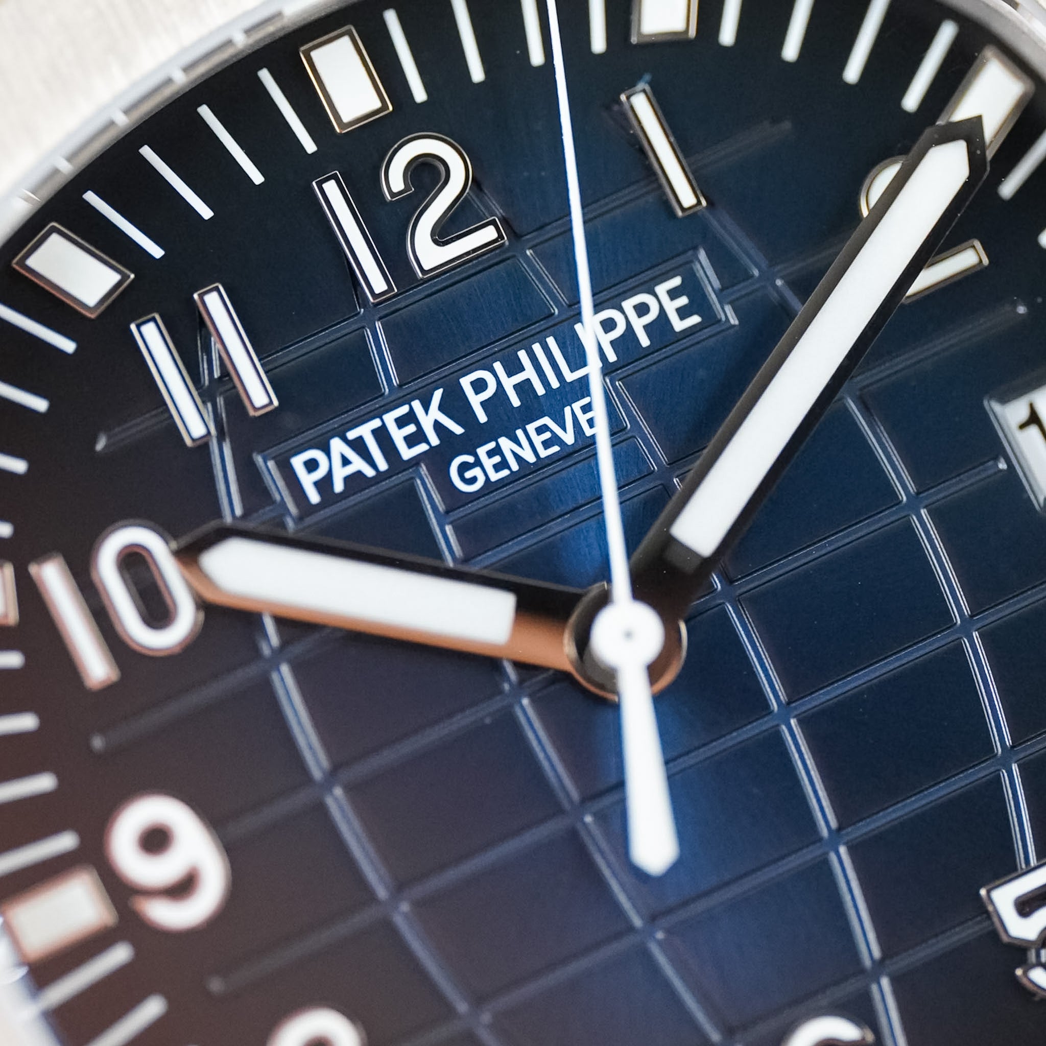 Close-up shot of a Patek Philippe watch dial with a textured, deep blue color, white hands and hour markers, and the Patek Philippe logo visible