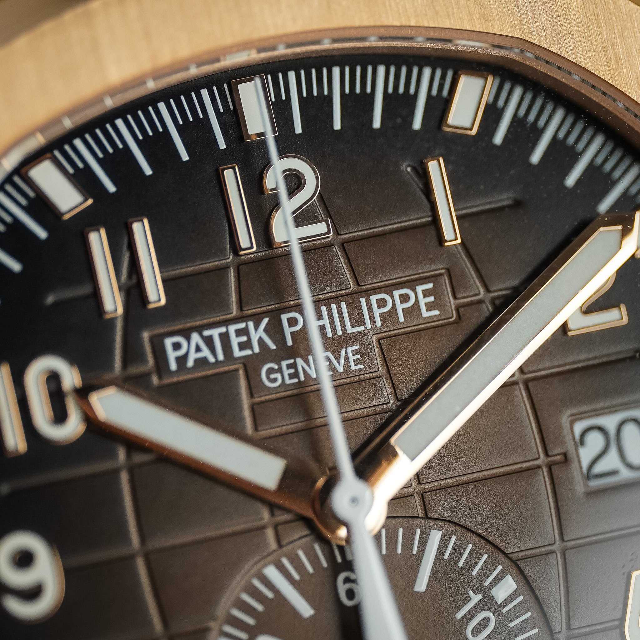 A closeup of a brown watch dial with a rose gold case, a Patek PPhilippe logo, and off-white hands and hour markers.