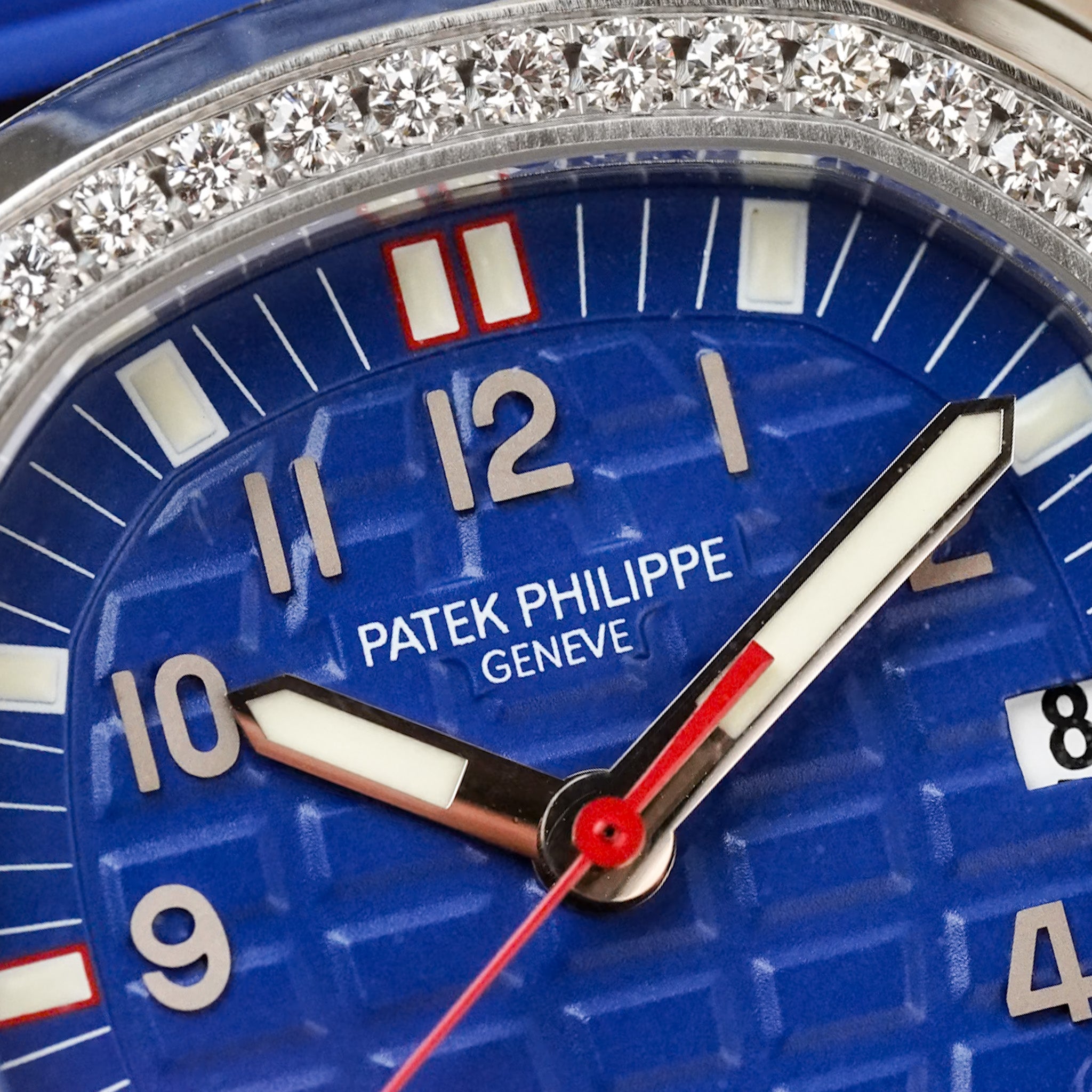 Closeup of a A stainless steel Patek Philippe Aquanaut with a textured blue dial featuring white arabic numerals and red accents, and a diamond bezel
