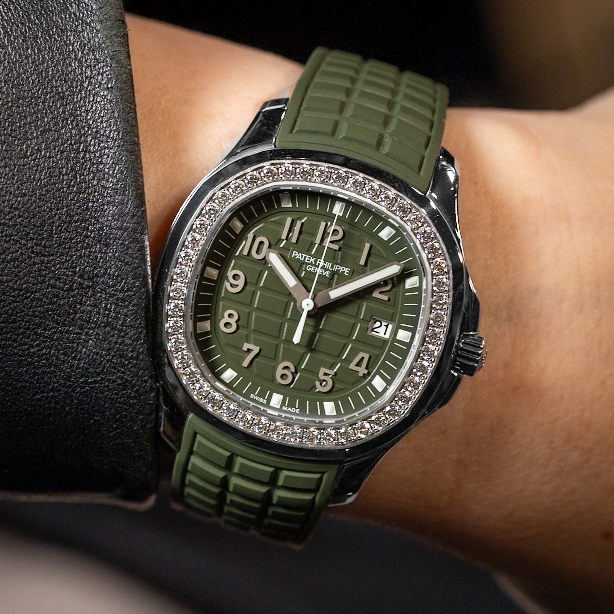 A wristwatch with an olive green textured dial and matching green strap, worn on a person's wrist. The watch has a steel bezel encrusted with diamonds and silver-tone numerals and hands.