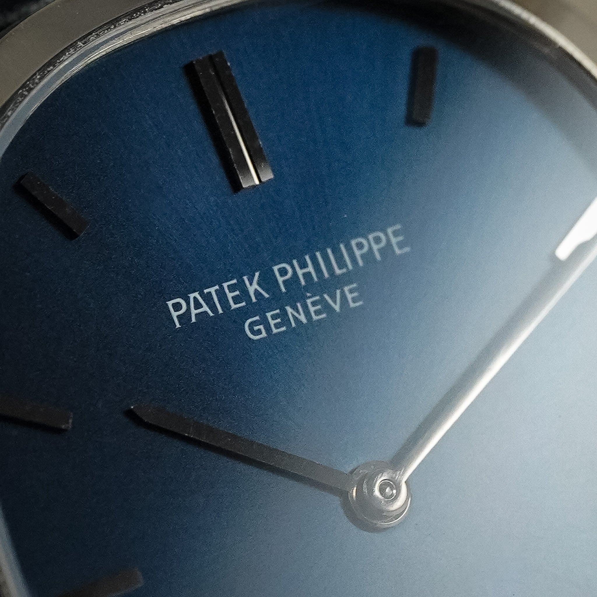Closeup of a Patek Philippe watch with a blue dial, white gold hands and hour markers, and the Patek Philippe Geneve brand name visible.