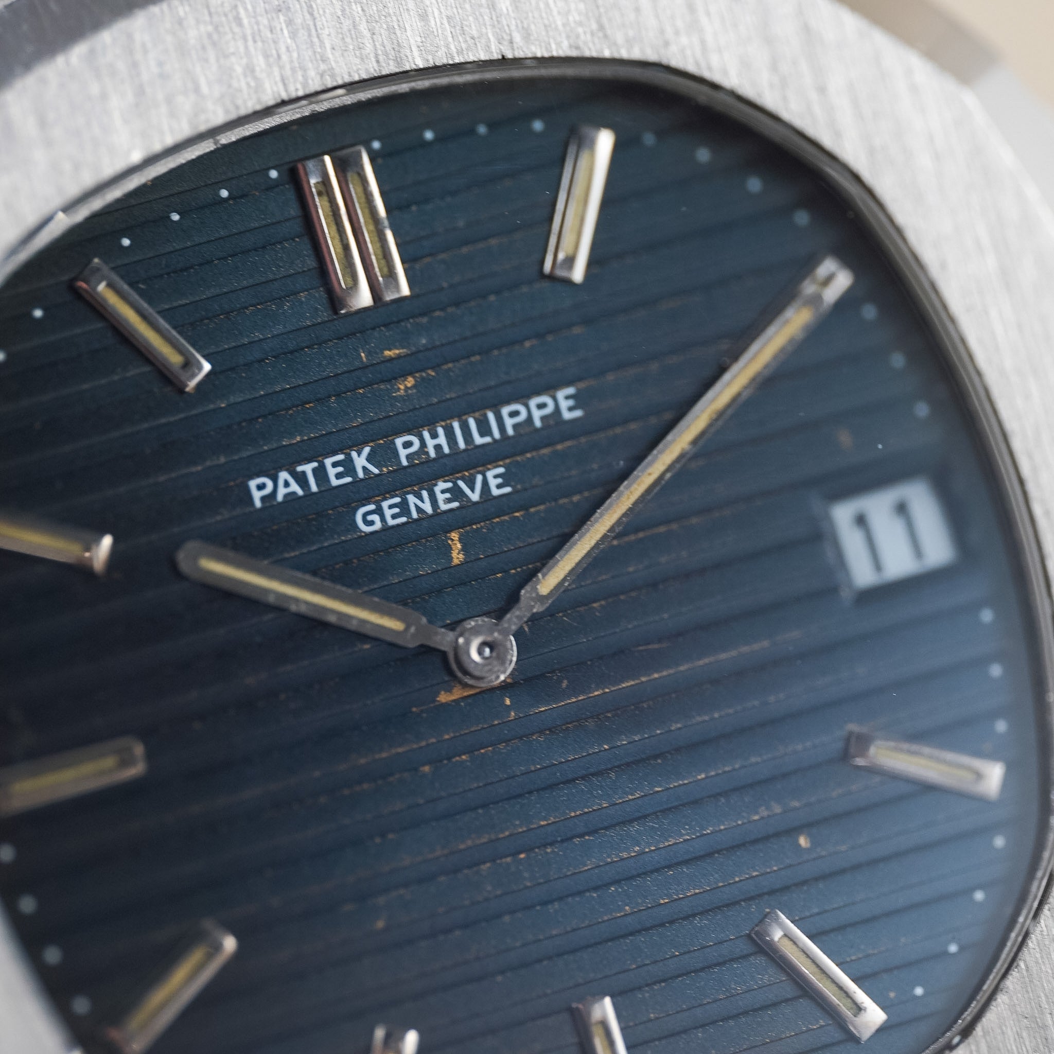 Close-up of a Patek Philippe Geneva watch dial with a dark blue ribbed face, silver baton hour markers, and a date window showing 11.