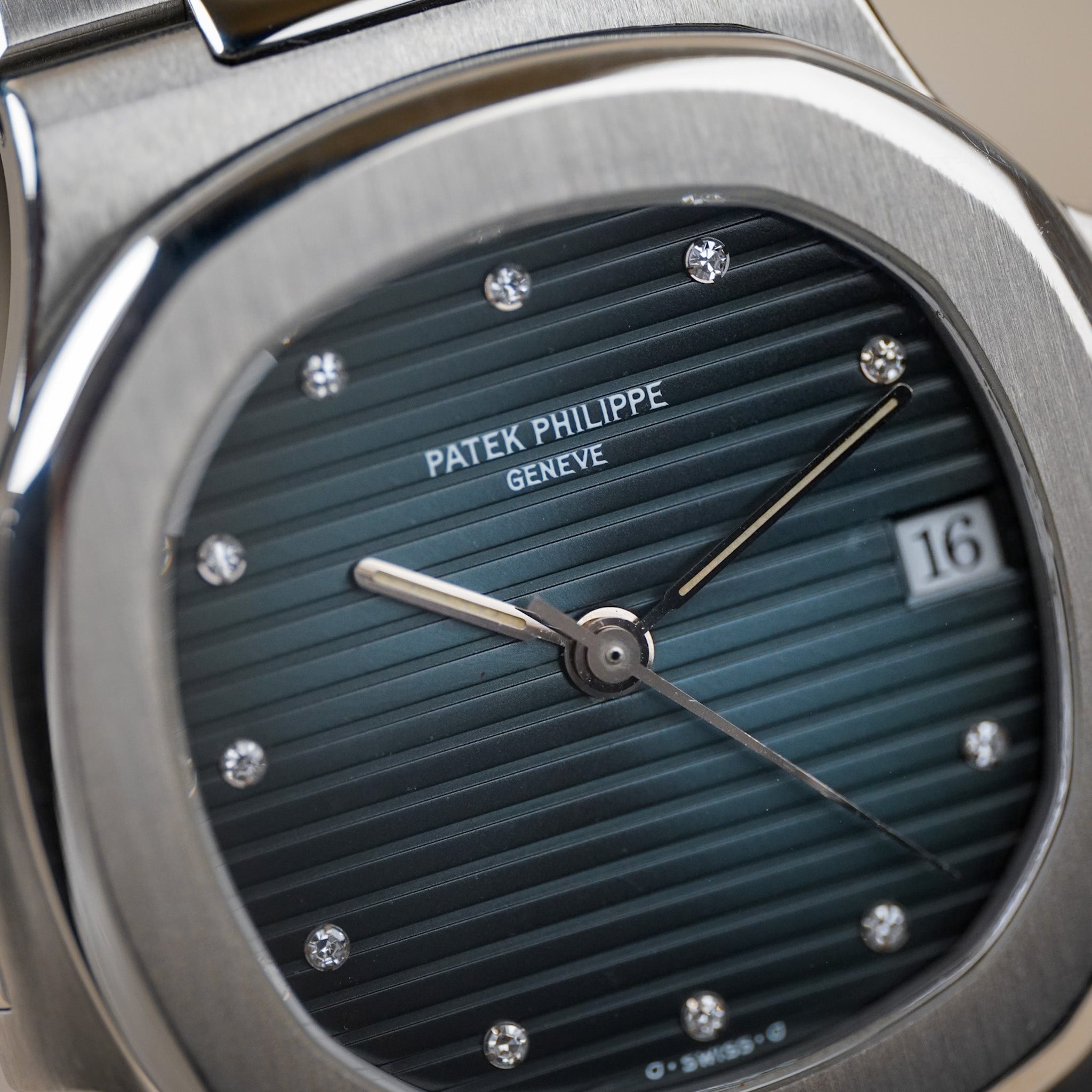 Closeup of a steel Patek Philippe Nautilus with a ribbed blue dial, diamond hour markers, and a date window showing "16"