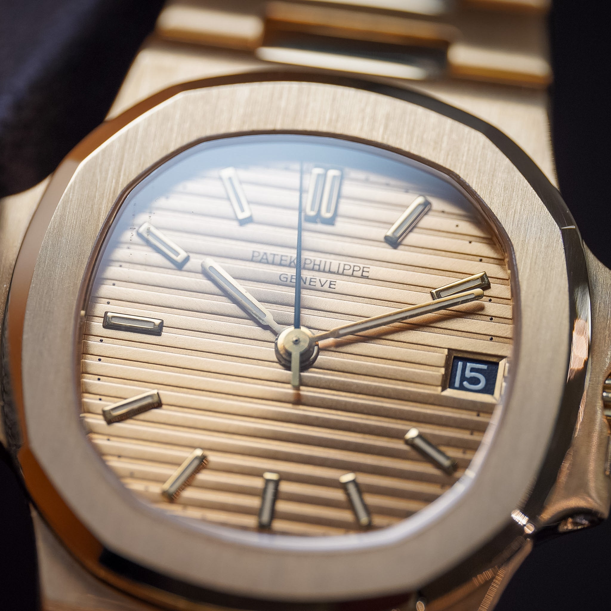Close-up of a Patek Philippe wristwatch with a brushed gold-toned octagonal bezel, a sunburst champagne dial with fluted lines, and a date window at 3 o'clock.