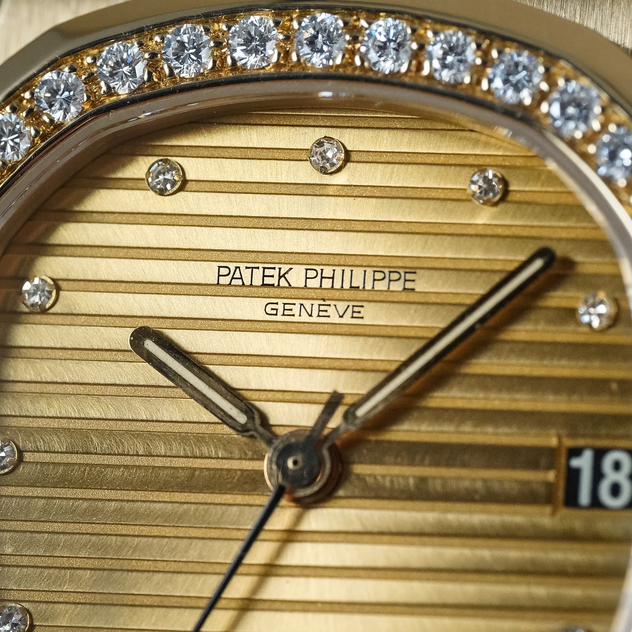 Close-up of a gold Patek Philippe wristwatch face with diamond hour markers, a gold bezel, and visible Patek Philippe Geneva branding.