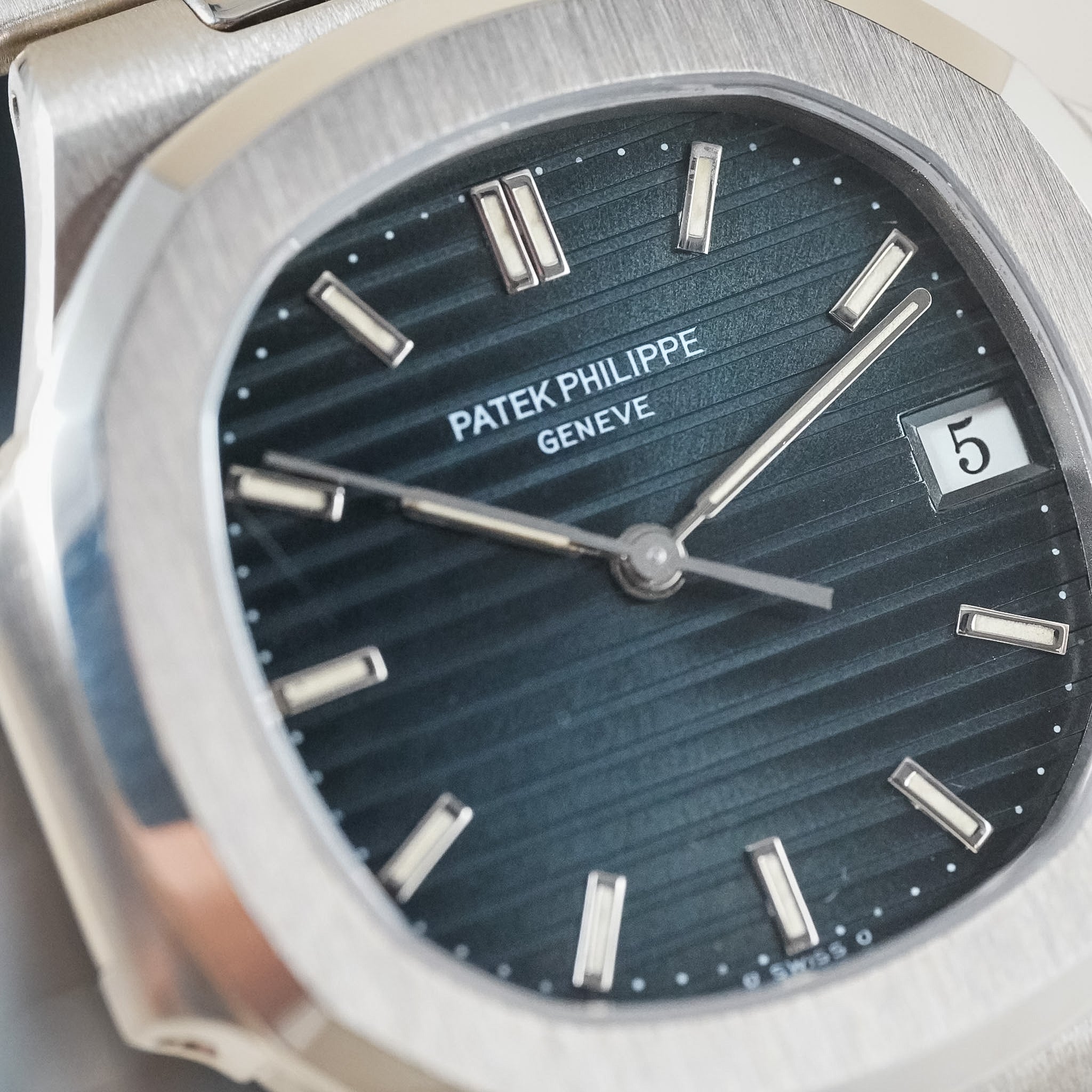 Close-up photo of a watch showing the logo Patek Philippe Geneve. The watch has a blue dial, white golf case, hands, and hour markers.