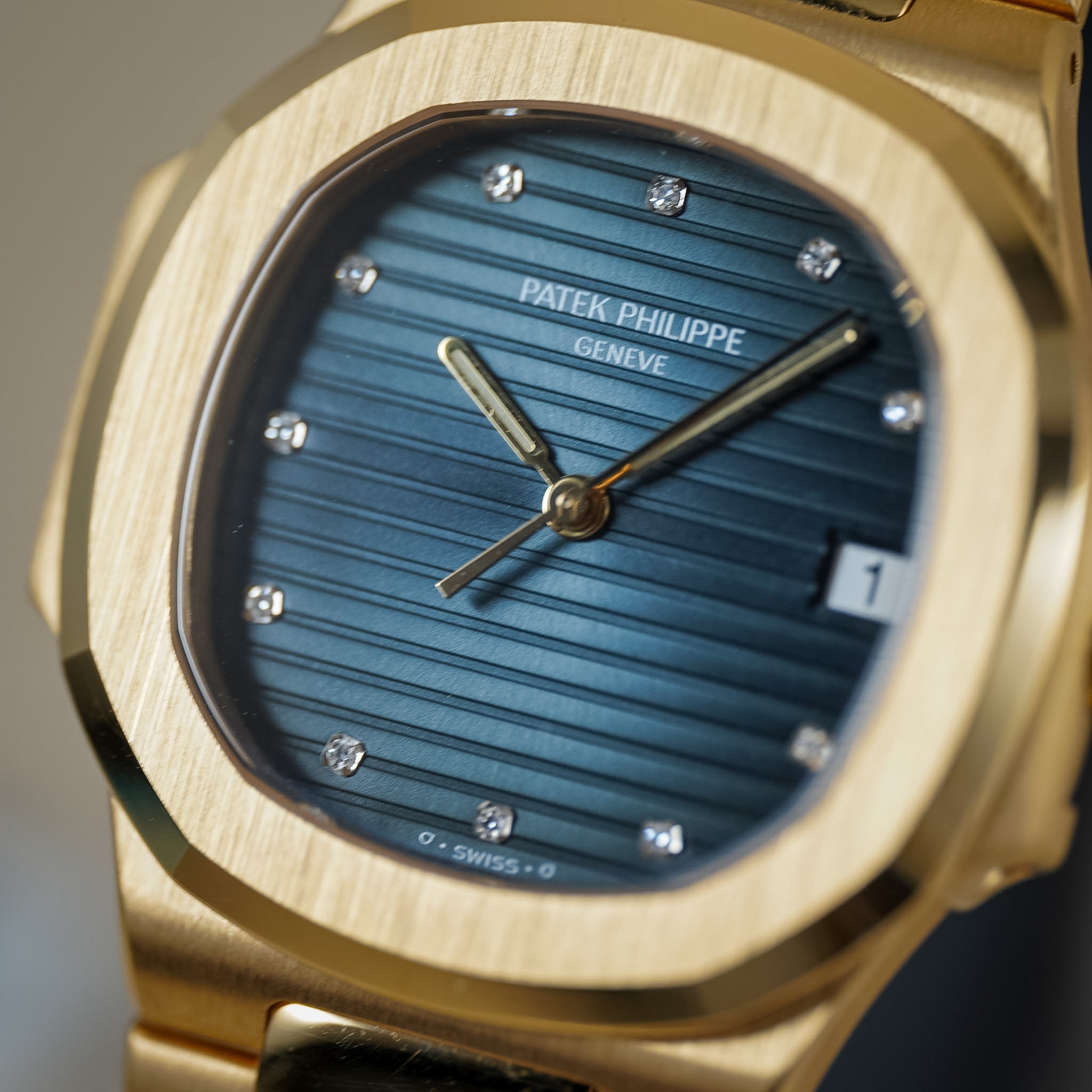 Close-up of a gold-tone Patek Philippe wristwatch with a blue striped dial and diamond hour markers.