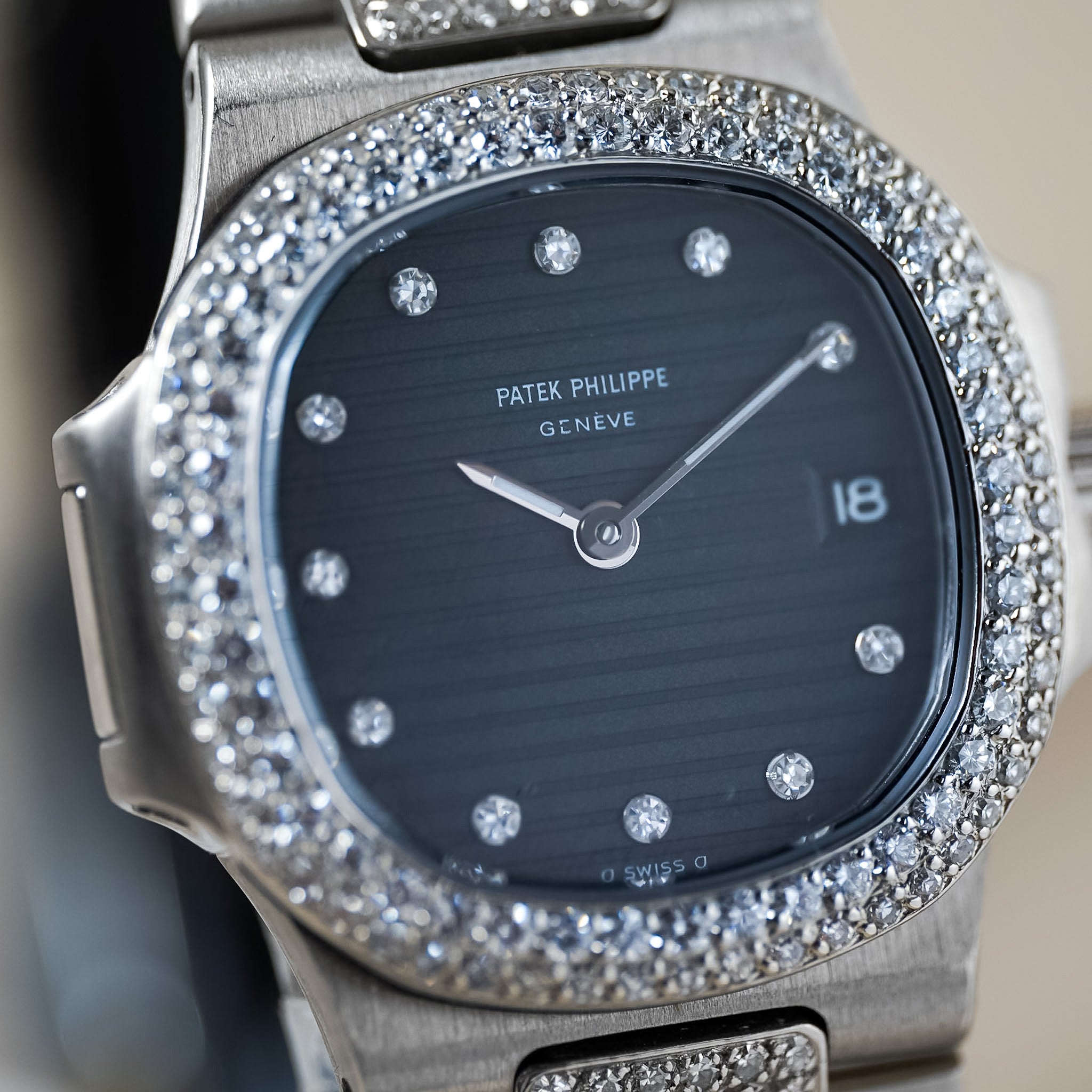 Close-up of a Patek Philippe Geneve wristwatch with a brushed silver-tone case, a diamond-paved bezel, and a dark blue sunburst dial with silver hands and diamond hour markers.