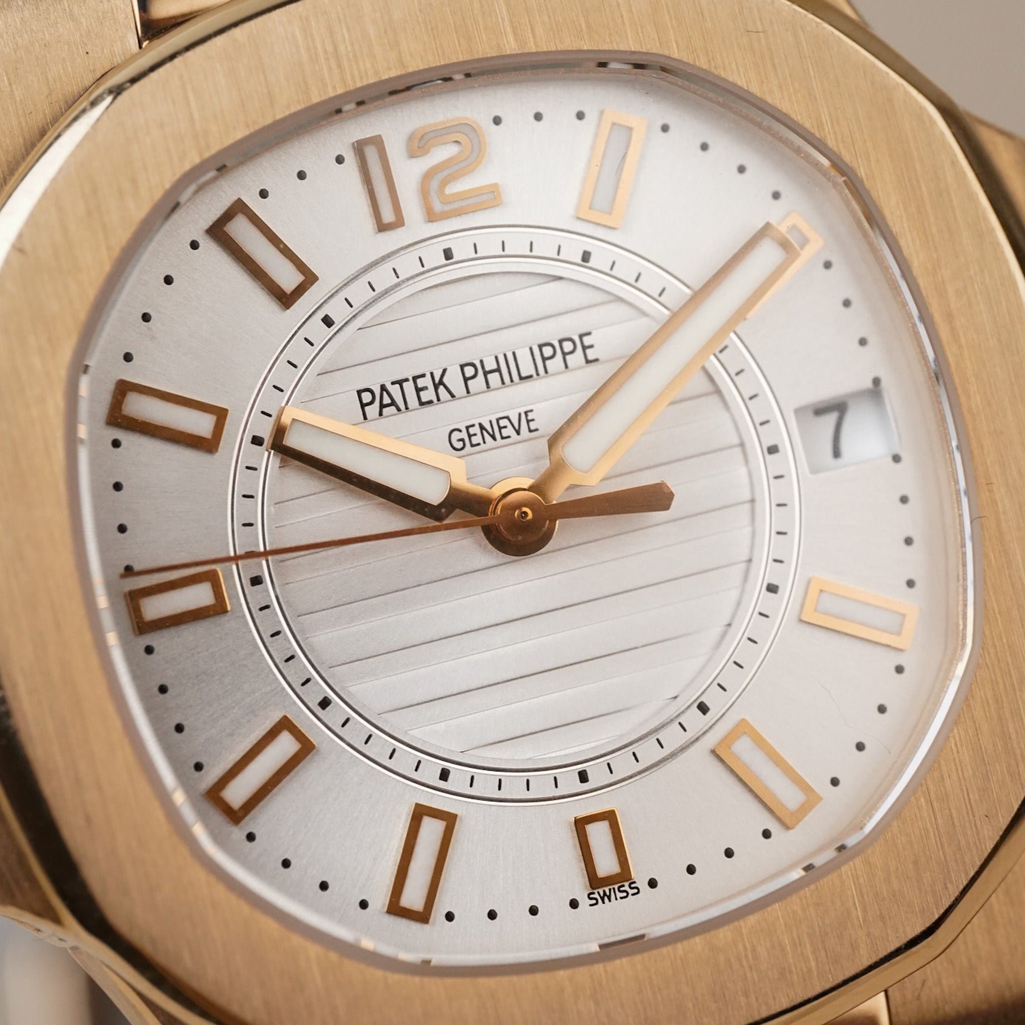 Close-up of a Patek Philippe wristwatch with a brushed gold-tone case, white dial, and gold-tone hour markers and hands.
