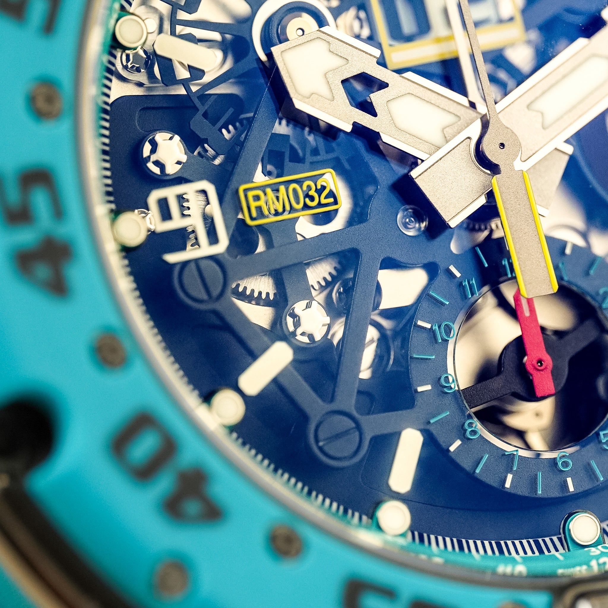 Close-up of a skeleton wristwatch with a turquoise bezel, blue dial, silver-tone hands and markers, and small yellow accents including a yellow RM032 badge and yellow side detail.