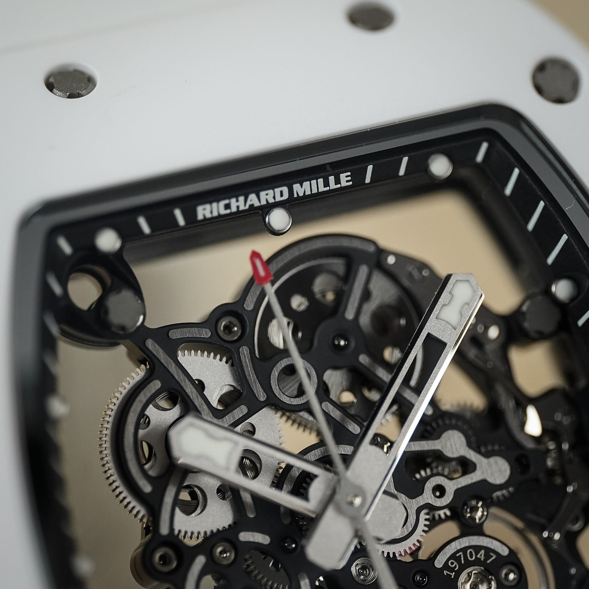 Close-up of a Richard Mille skeleton watch showing the intricate mechanical movement with silver and black components, white hands, and a white outer case.