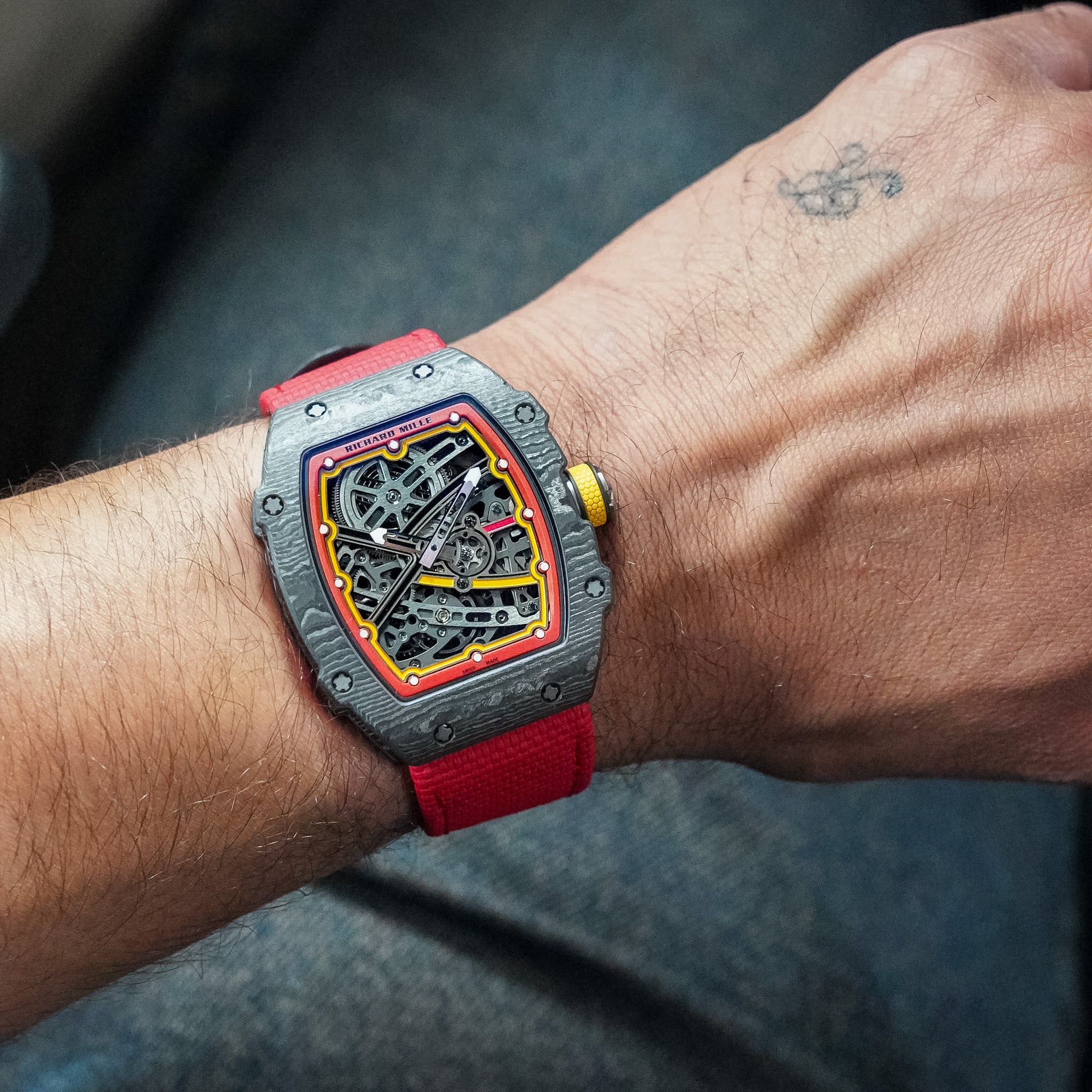 A Richard Mille watch with a skeleton dial, red strap, and red and yellow accents shot on a man's wrists