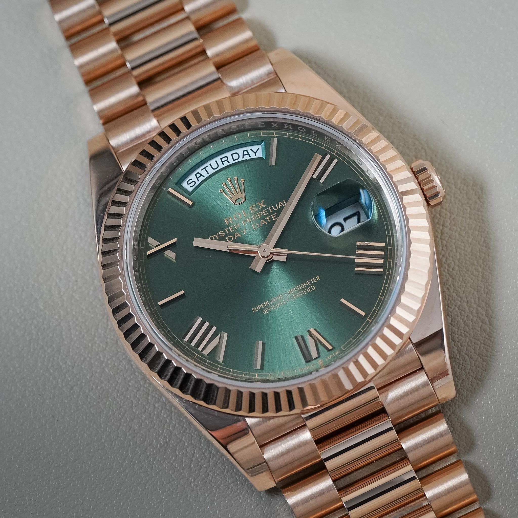 A Rolex Datejust wristwatch with a green sunburst dial, rose gold case, and matching rose gold Oyster bracelet, photographed close-up on a neutral gray background.