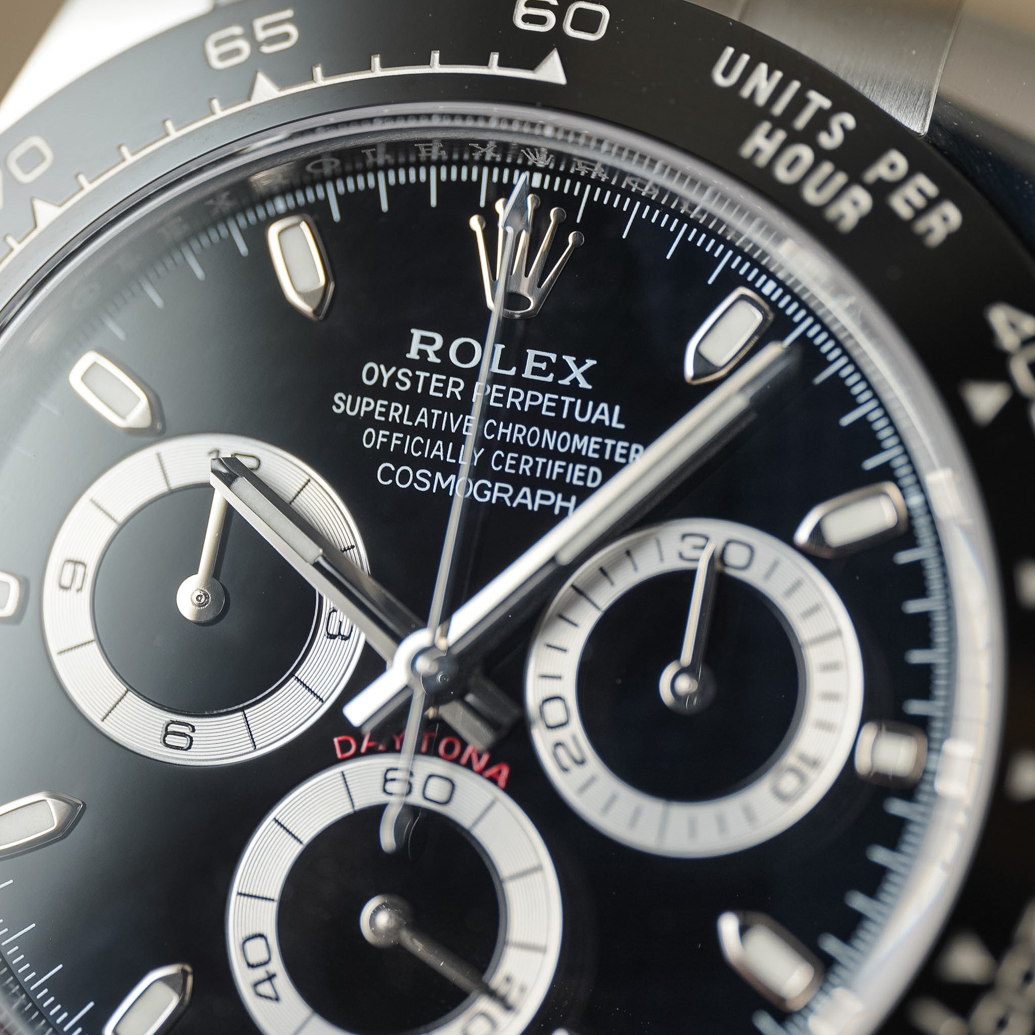 Close-up of a Rolex Daytona watch dial and bezel, showing the black chronograph face, silver-tone markers and hands, white subdials, and a black tachymeter bezel.