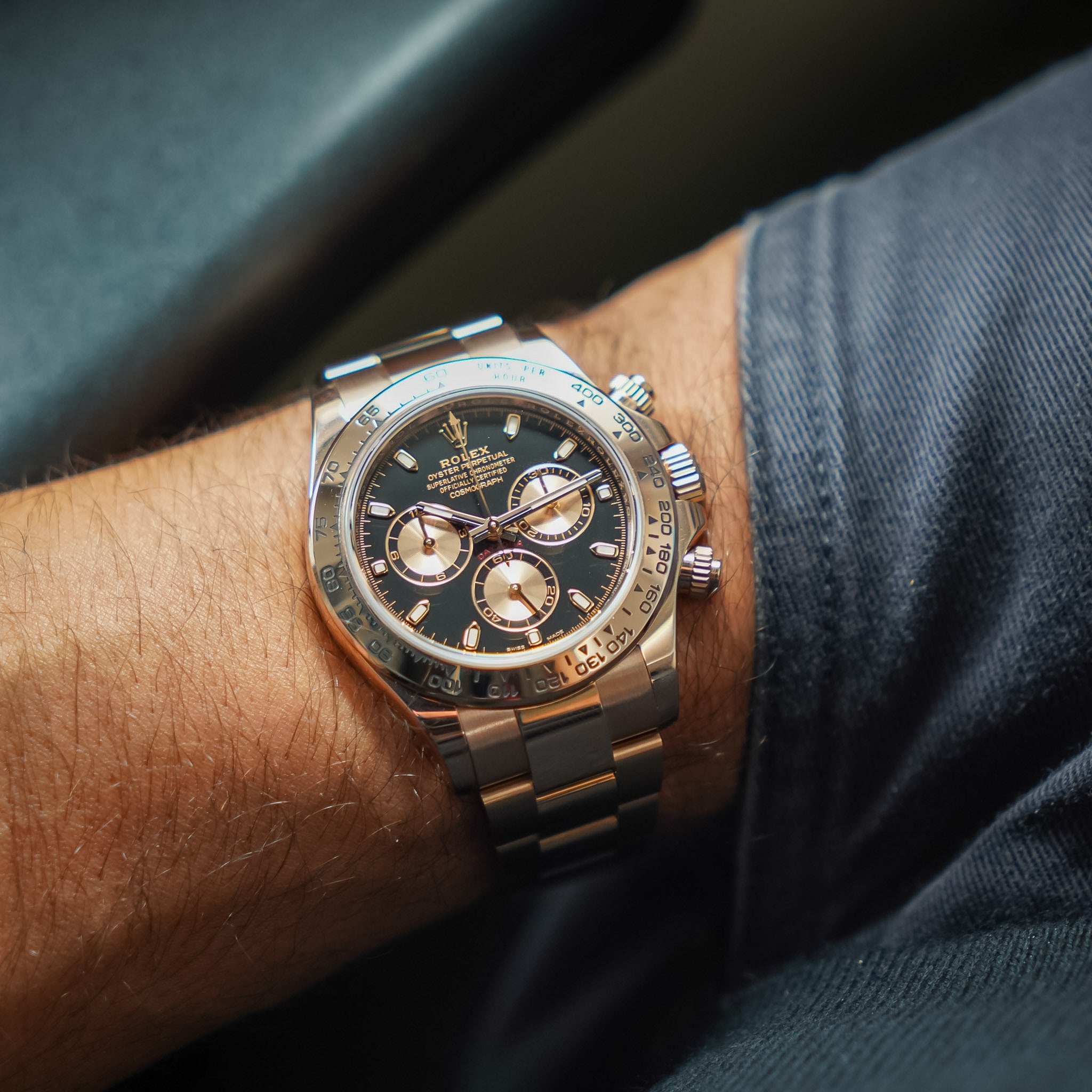 A close-up of a Rolex Daytona watch with a black dial and rose gold bracelet, worn on a person's wrist.