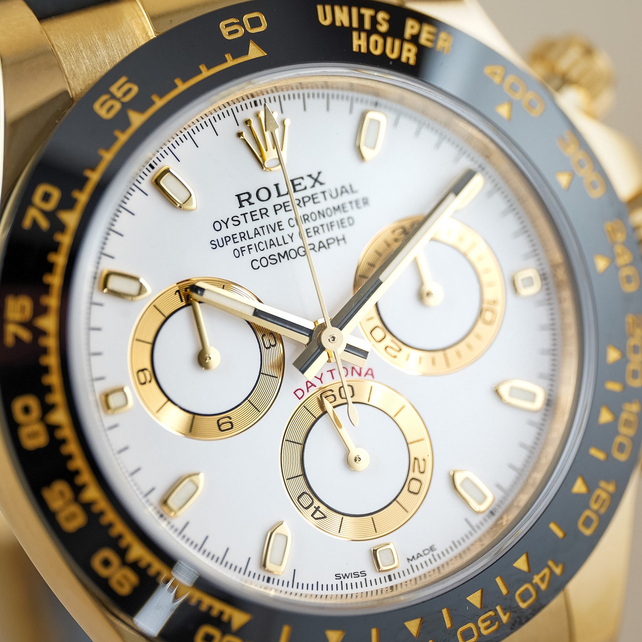 Close-up of a Rolex Daytona watch with a gold case, white dial, black bezel, and gold subdials.