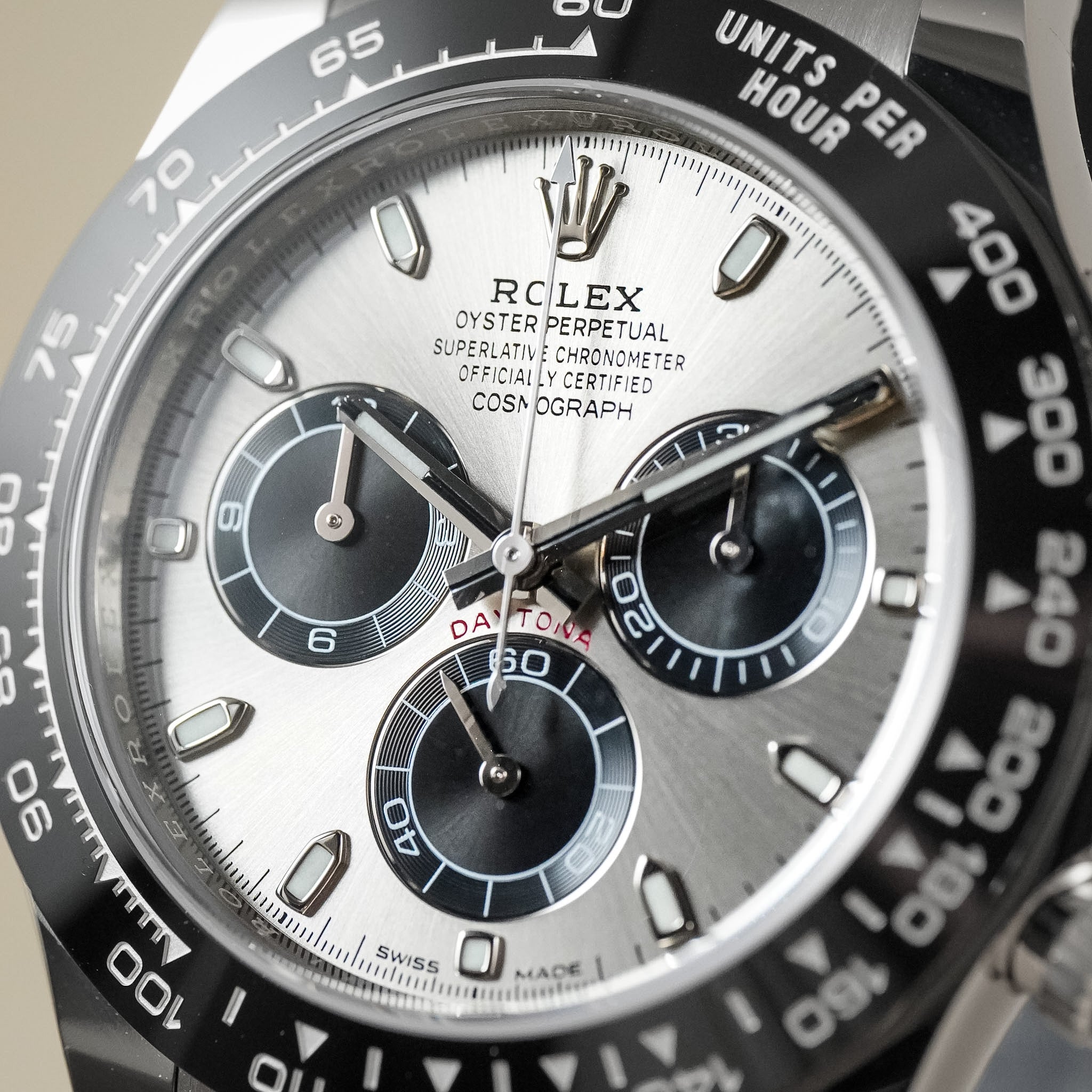 Close-up of a Rolex Daytona watch dial and bezel, showing a silver chronograph face with black subdials and a black tachymeter bezel.