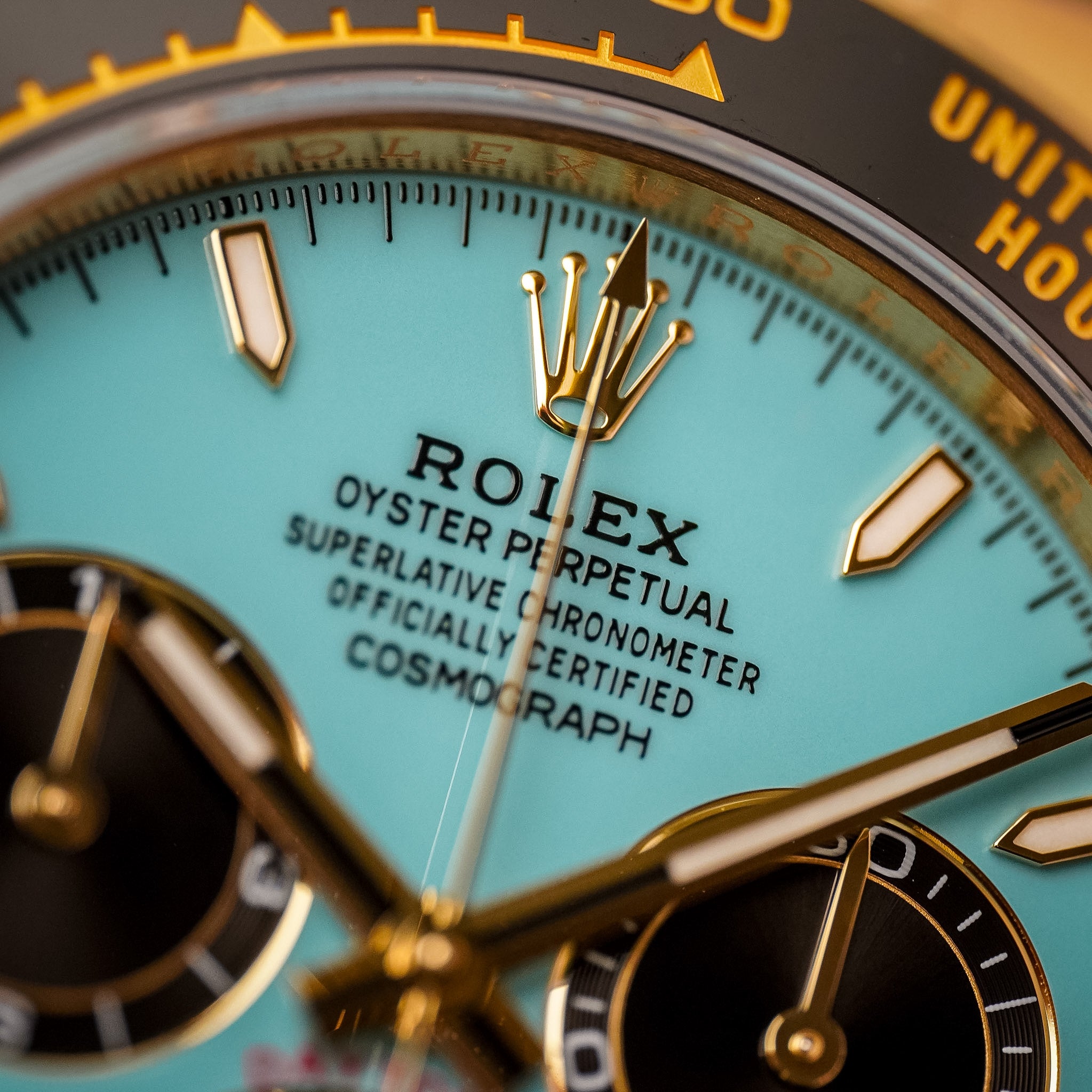 Closeup of a yellow gold Rolex Daytona with a turquoise dial and black bezel and subdials 