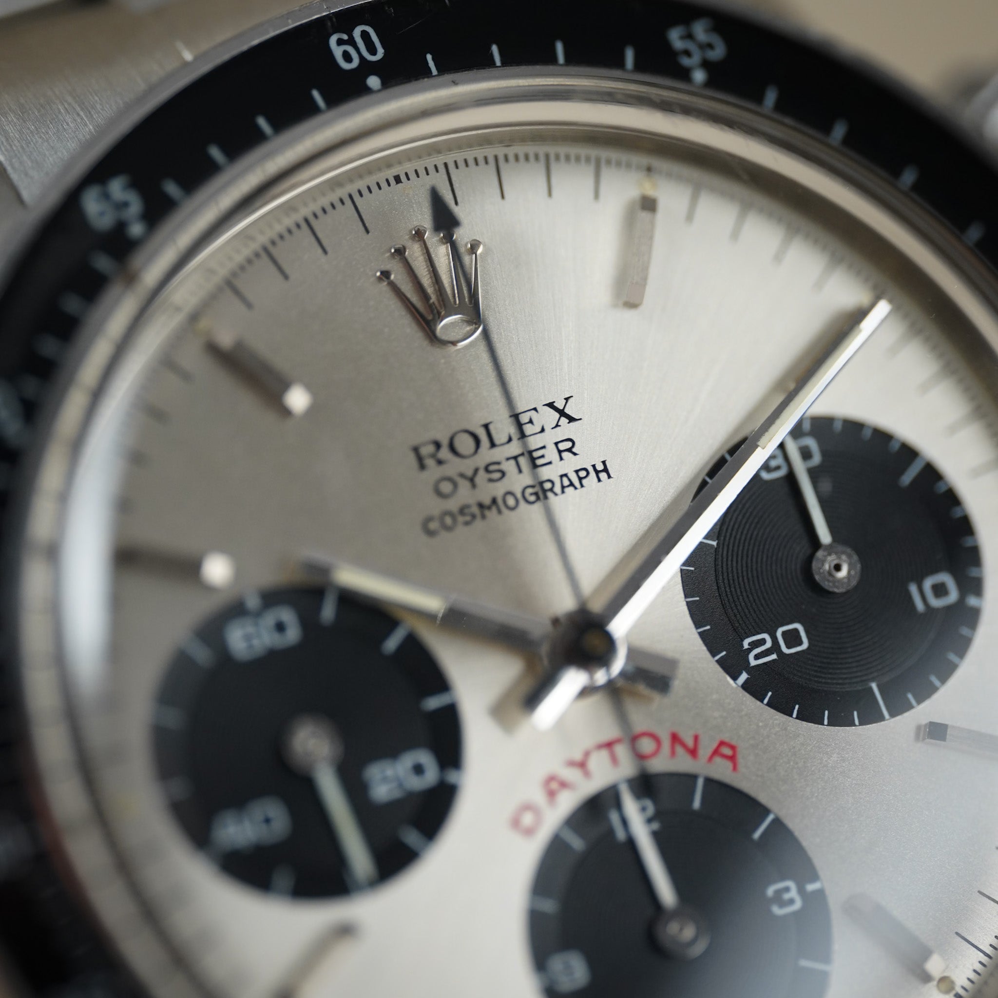 Close-up of a Rolex Oyster Cosmograph Daytona watch dial with a silver-toned sunburst finish, black subdials, a black bezel, and silver hands.