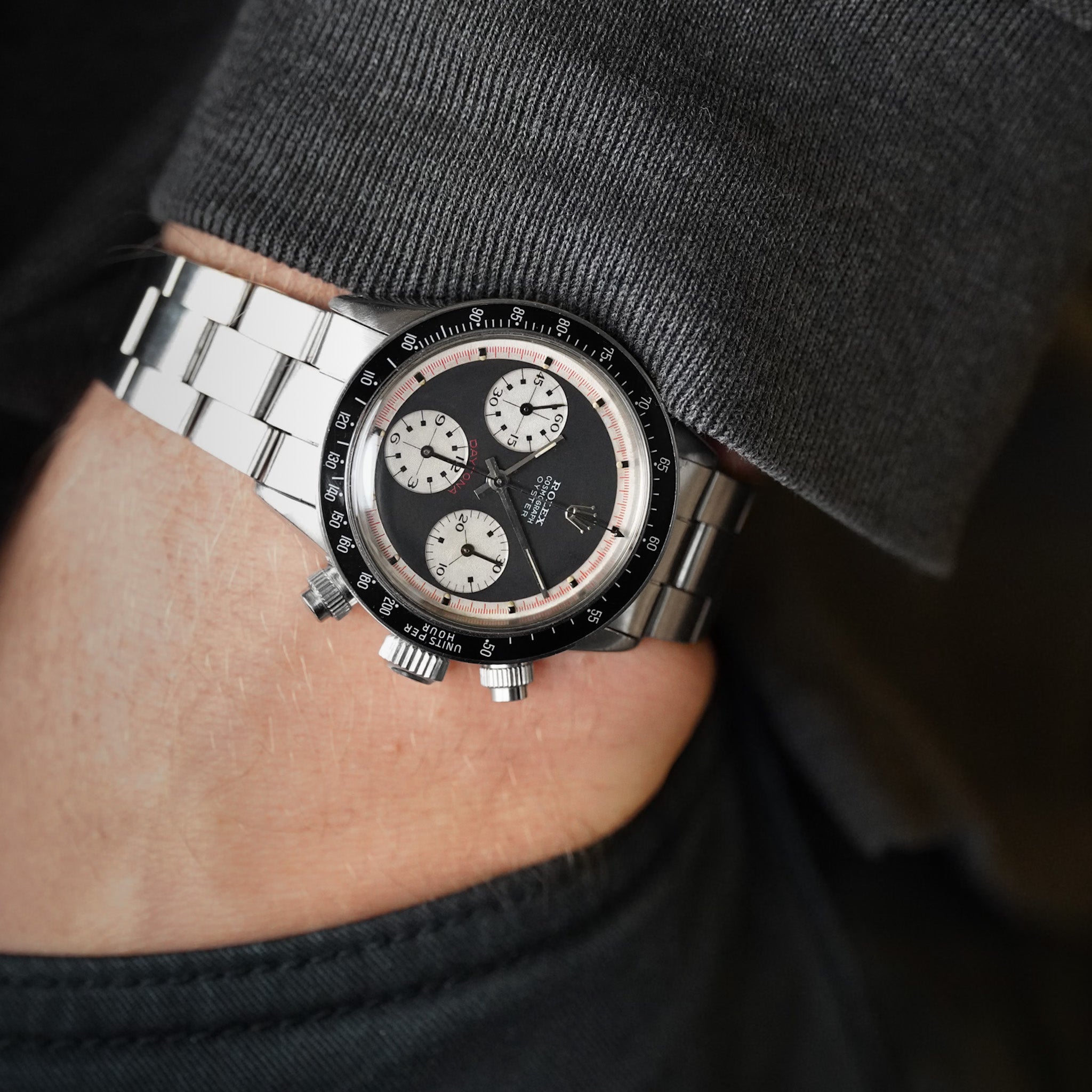 A black dial vintage Rolex Daytona in steel with a black bezel, white subdials, and red accents, shot on a man's wrist wearing dark clothing.