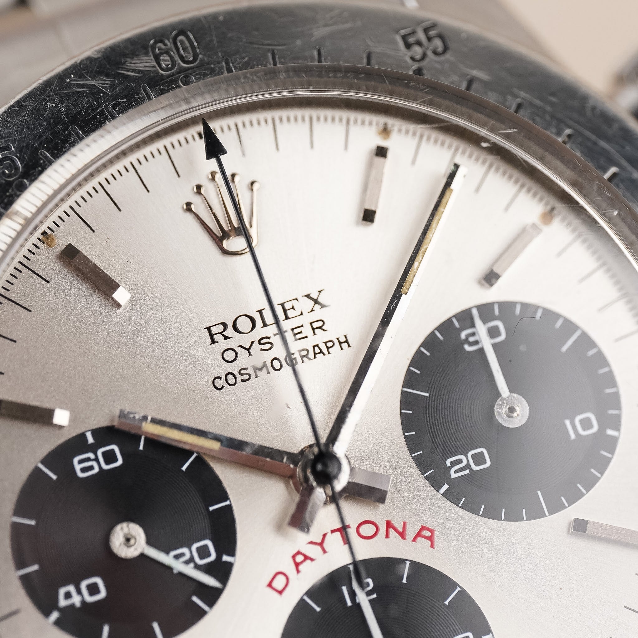 Closeup of a A vintage Rolex chronograph watch with a steel case, steel bezel, and silver dial with black subdials. One can read the words Rolex Oyster Cosmograph and Daytona.