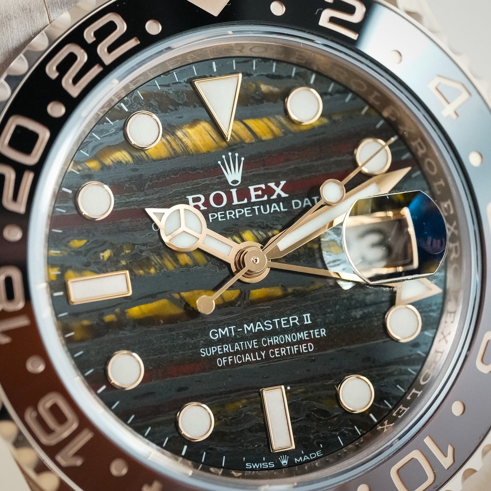 Close-up of a Rolex GMT-Master II Perpetual Date watch with a dark marbled dial, gold-tone hands and markers, and a brown and black bezel.