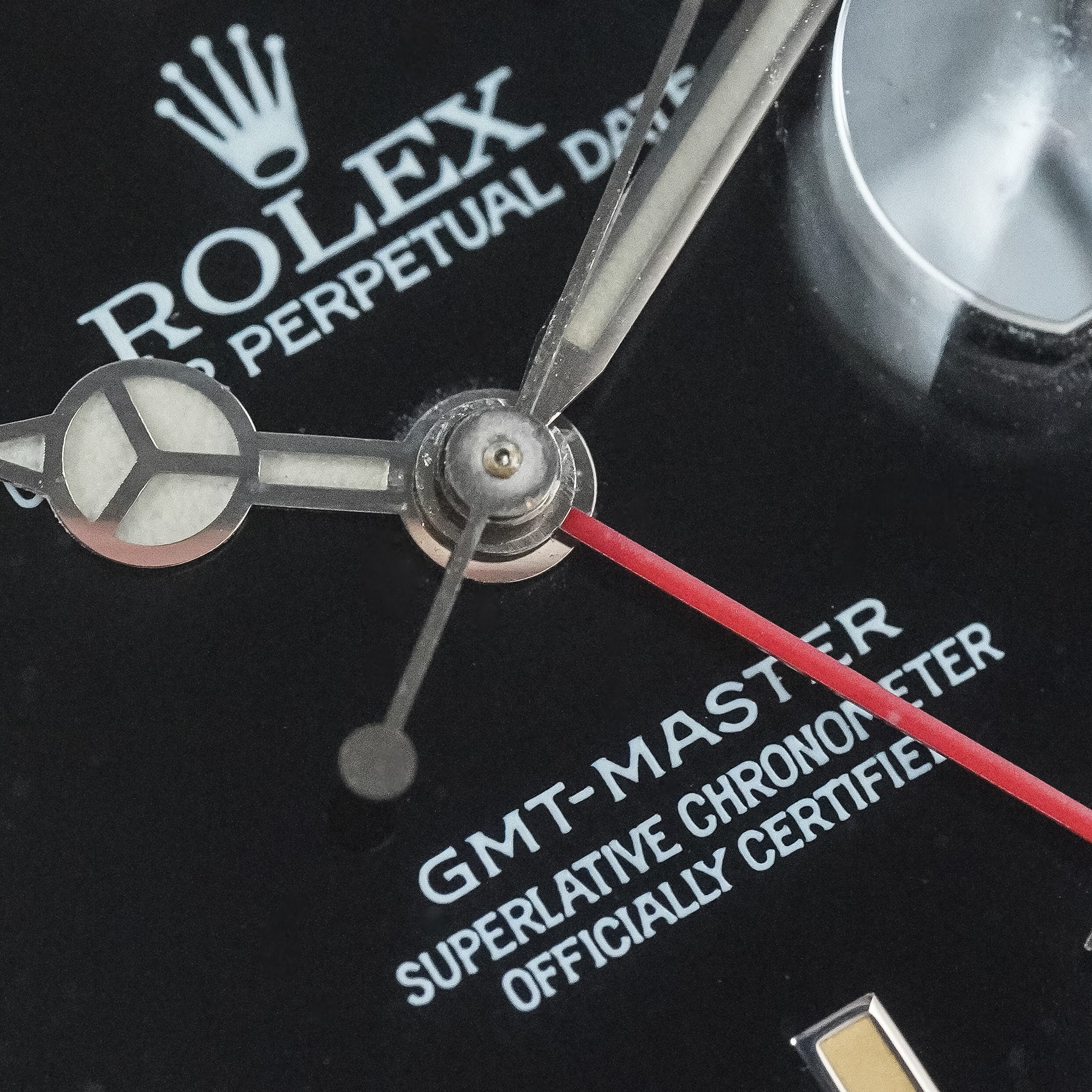 Close-up of a Rolex GMT-Master watch dial with silver-tone hands, a red second hand, white Rolex branding and text on a black case, and part of a clear crystal.