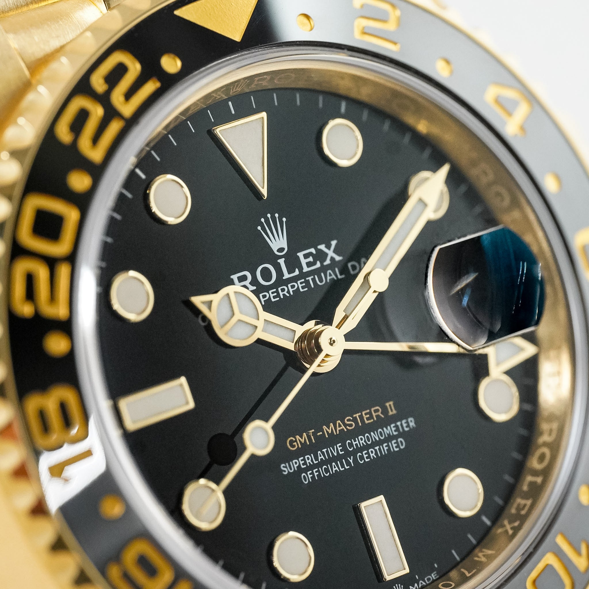 Close-up of a Rolex GMT-Master II watch dial and bezel, showing a black dial with gold-tone hands, luminous hour markers, and a gold-and-black rotating bezel.