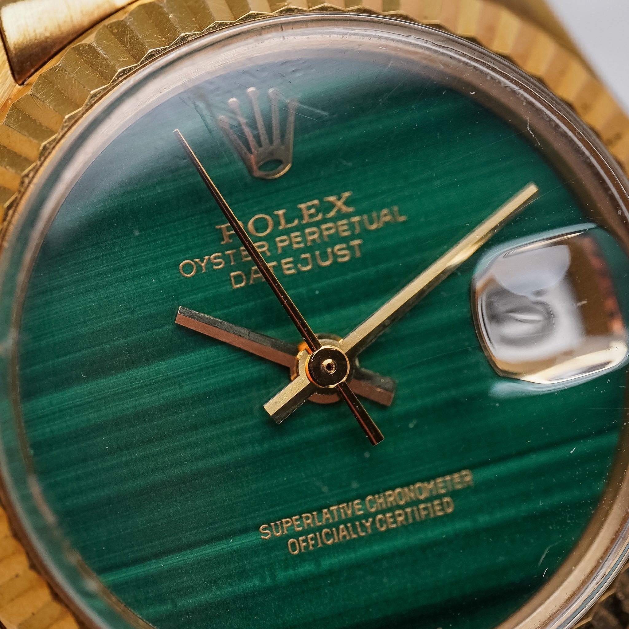 A close-up of a yellow gold ladies Rolex Oyster Perpetual with a vibrant green malachite stone dial, gold bezel, and gold hands.