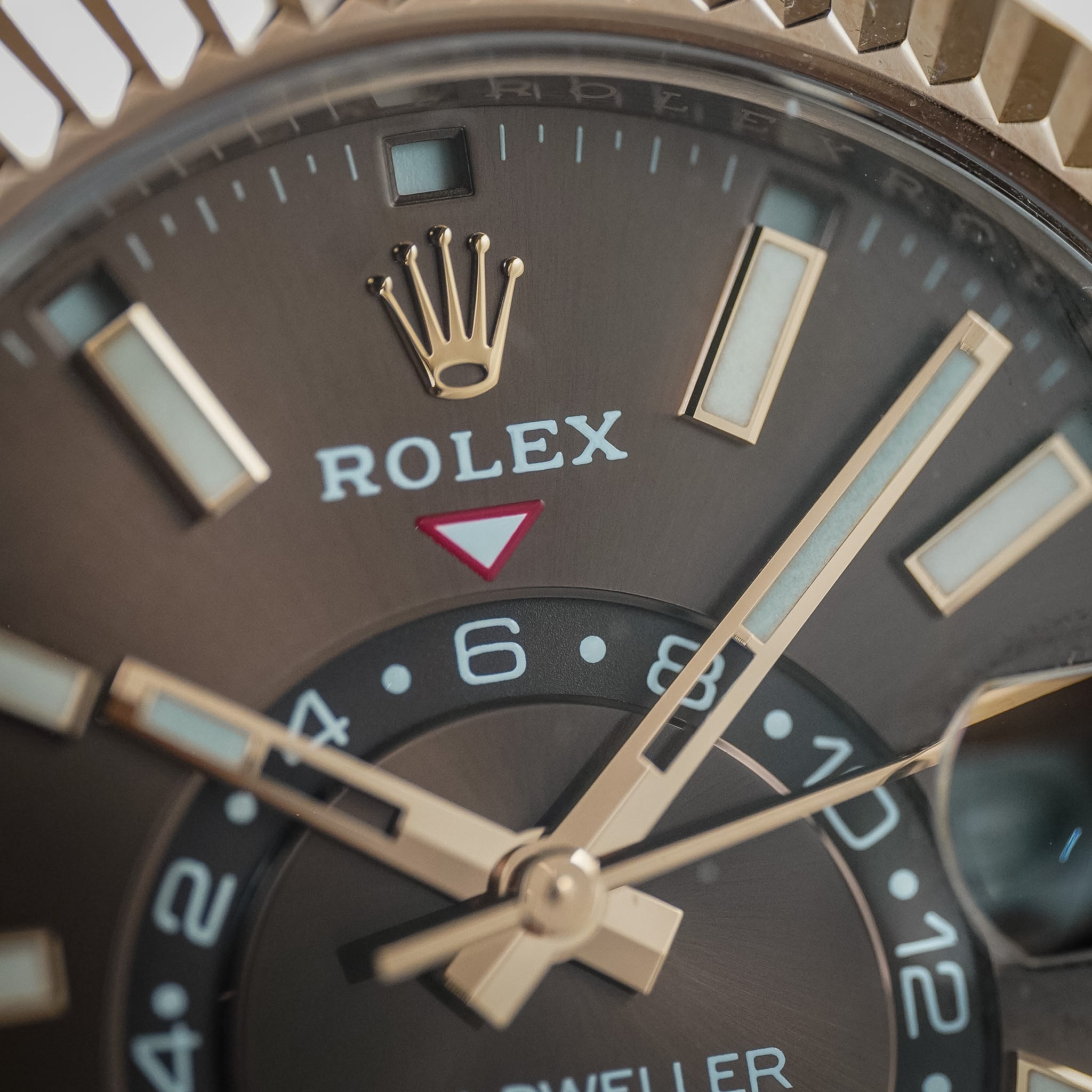 A close-up image of a Rolex Sky-Dweller dial. This dial is chocolate brown with rose gold accents and a Rolex logo at the top.