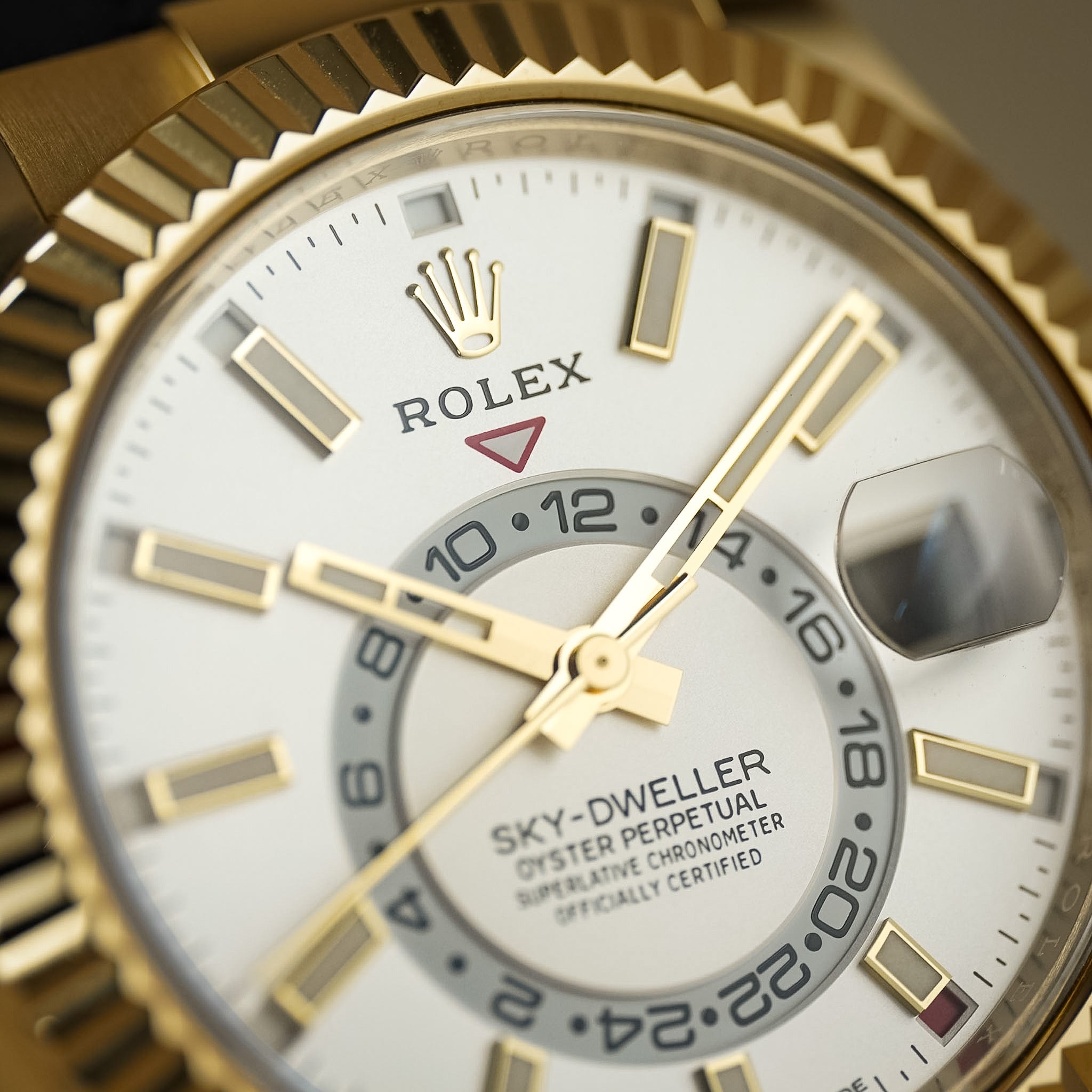Close-up of a Rolex Sky-Dweller Oyster Perpetual Chronometer watch with a gold fluted bezel, white dial, and gold-toned markers and hands.