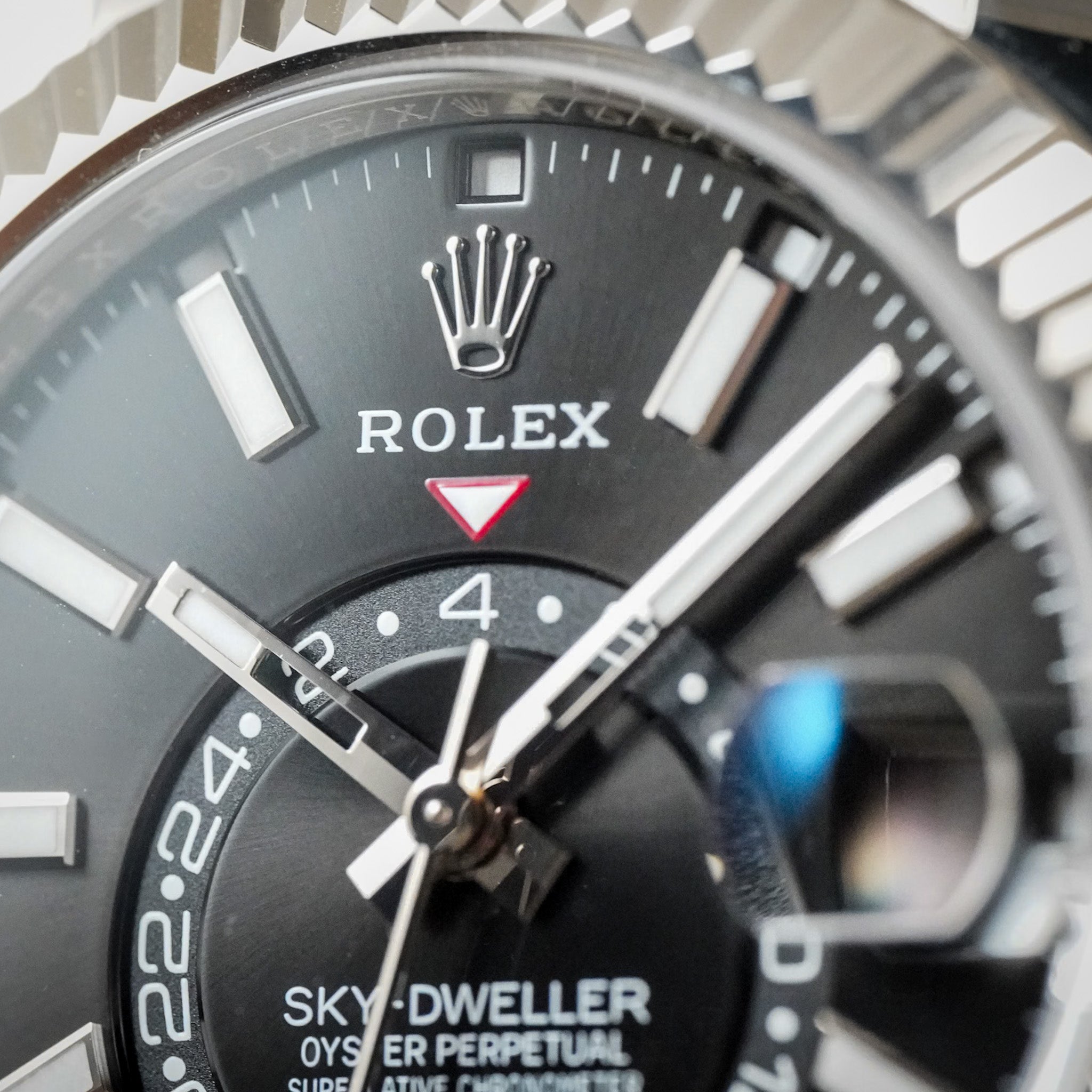 Close-up of a Rolex Sky-Dweller Oyster Perpetual watch dial, showing the black textured bezel, silver-tone hour markers, black dial with white text, and the Rolex crown logo.