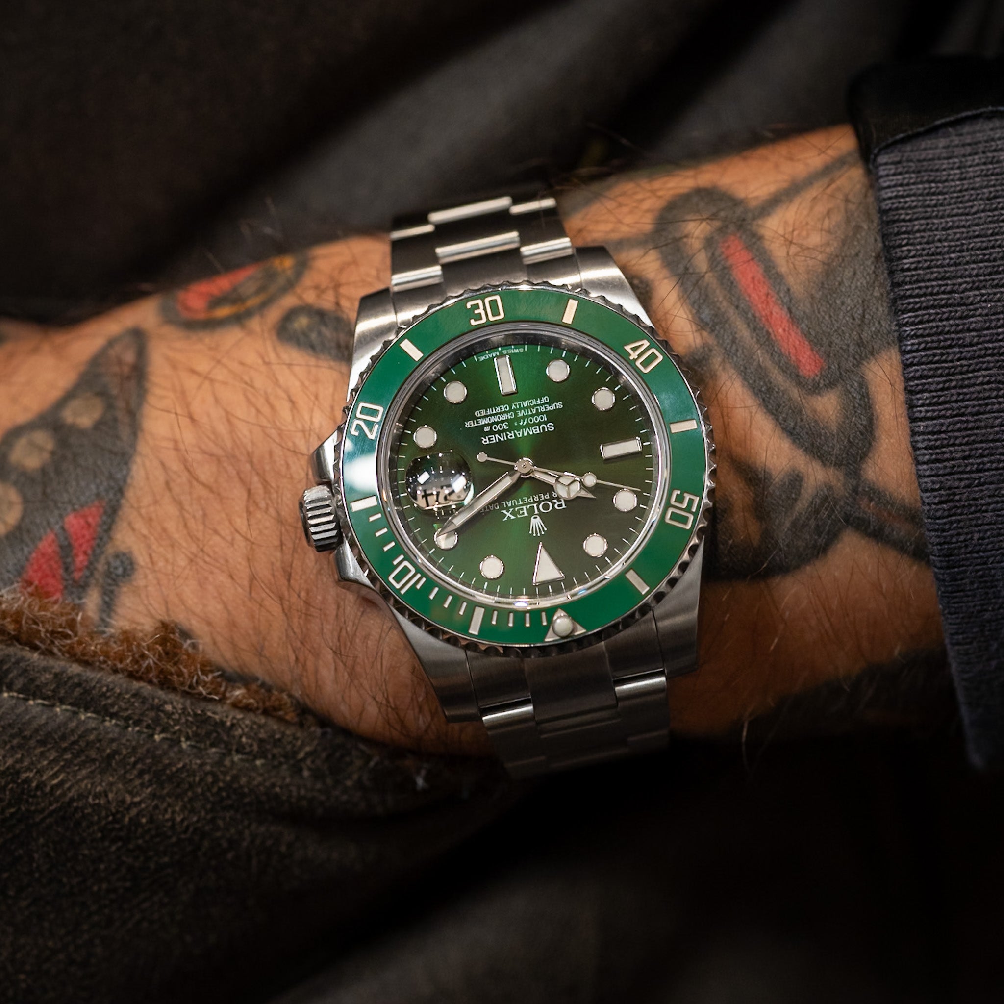 Green and silver watch on a tattooed wrist