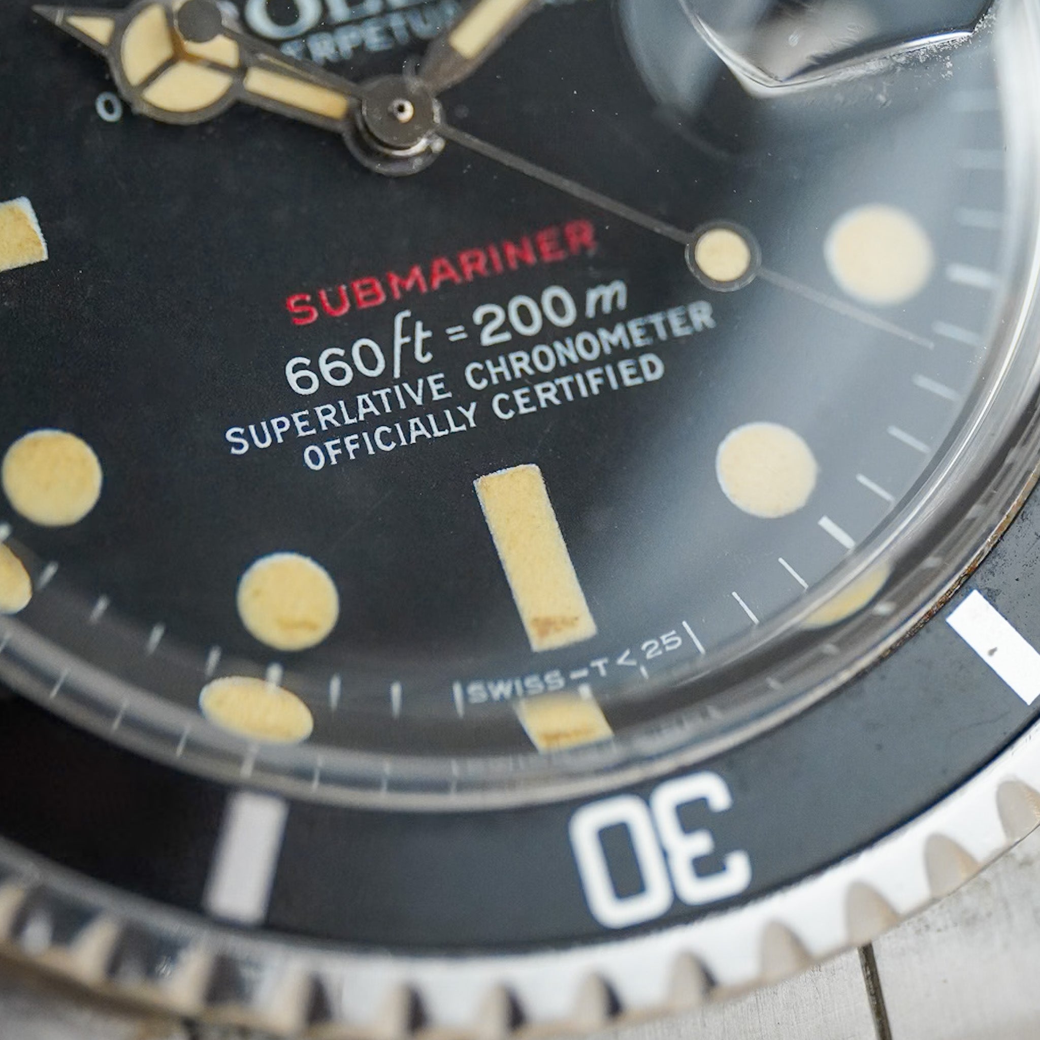 Close-up of a vintage Submariner watch dial with a black face, cream-colored hour markers, red 'SUBMARINER' text, and a black rotating bezel.