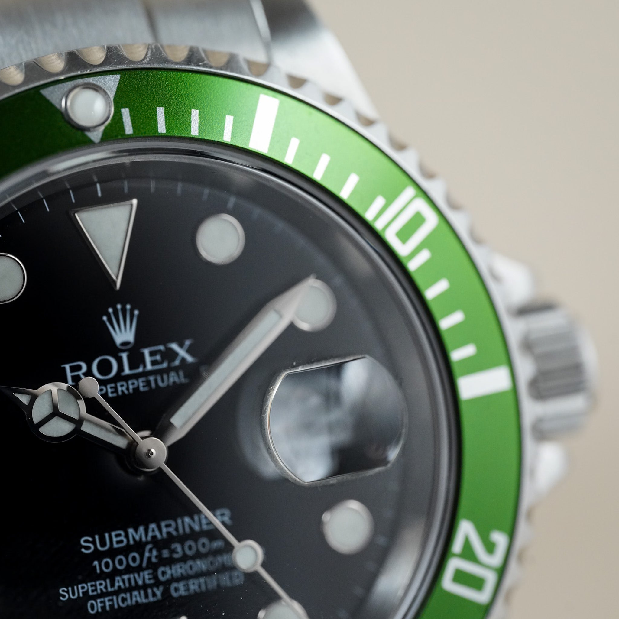 Close-up of a Rolex Submariner watch featuring a black dial, silver-tone stainless steel case, and a distinctive green aluminum bezel with white markings.