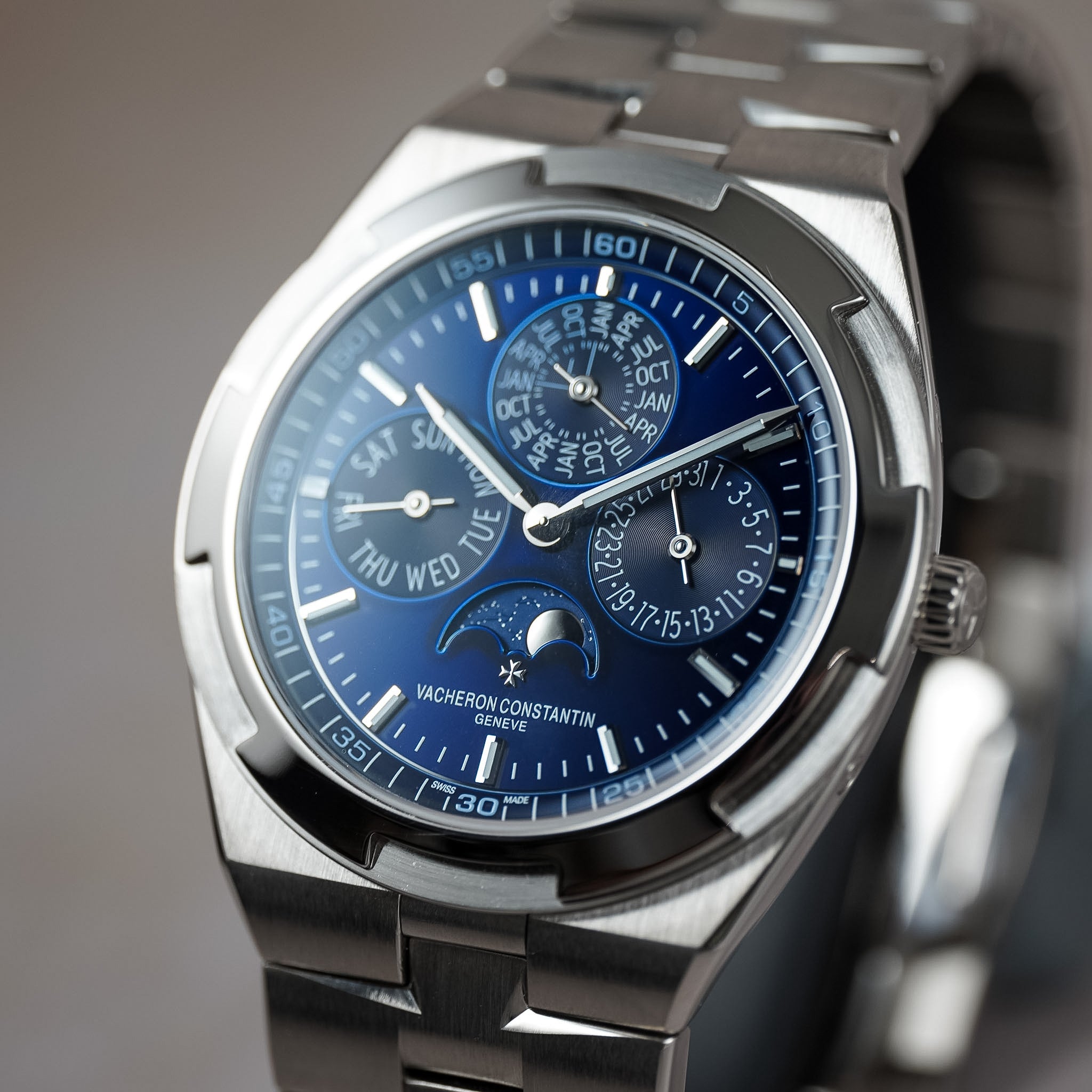 A close-up shot of a Vacheron Constantin Grandmaster watch featuring a stainless steel link bracelet, a silver-toned case, and a deep blue dial with multiple subdials and a moon phase indicator.