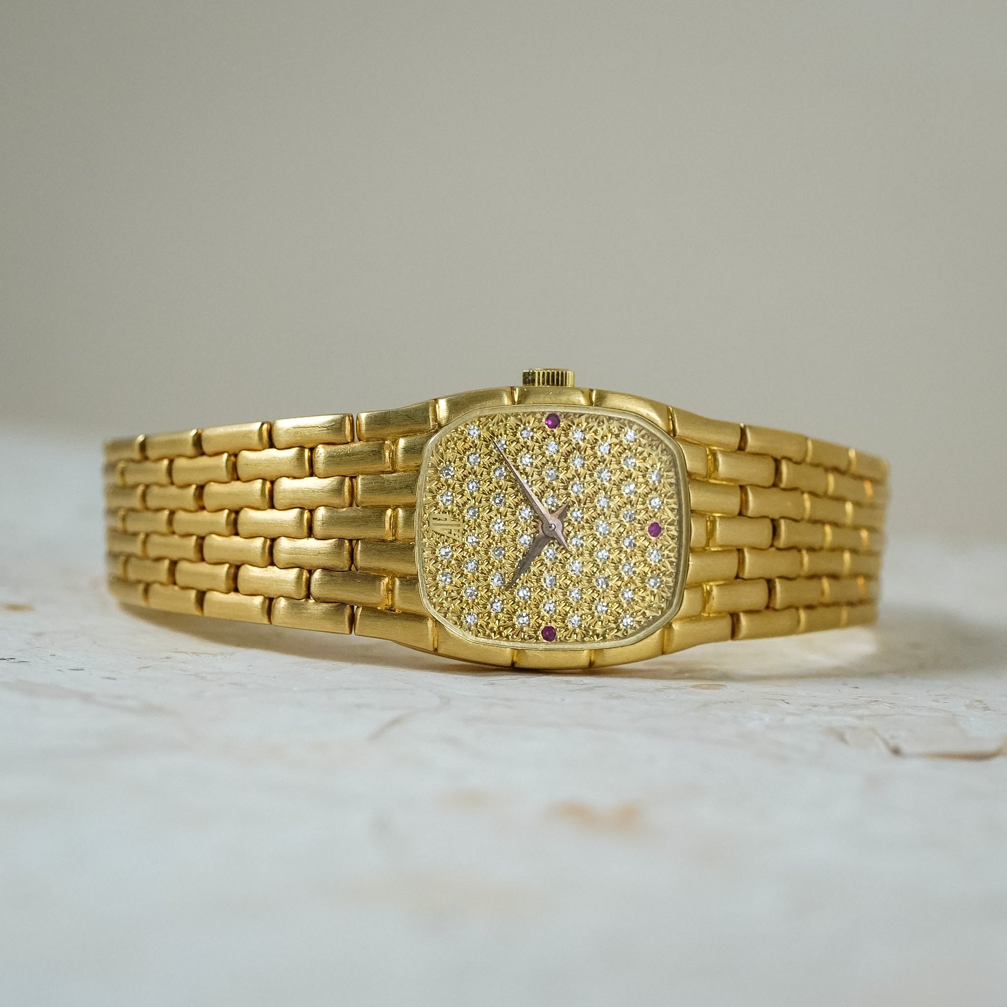 A gold watch with a pavé diamond dial and matching link bracelet, photographed lying sideways on a textured light gray stone surface.