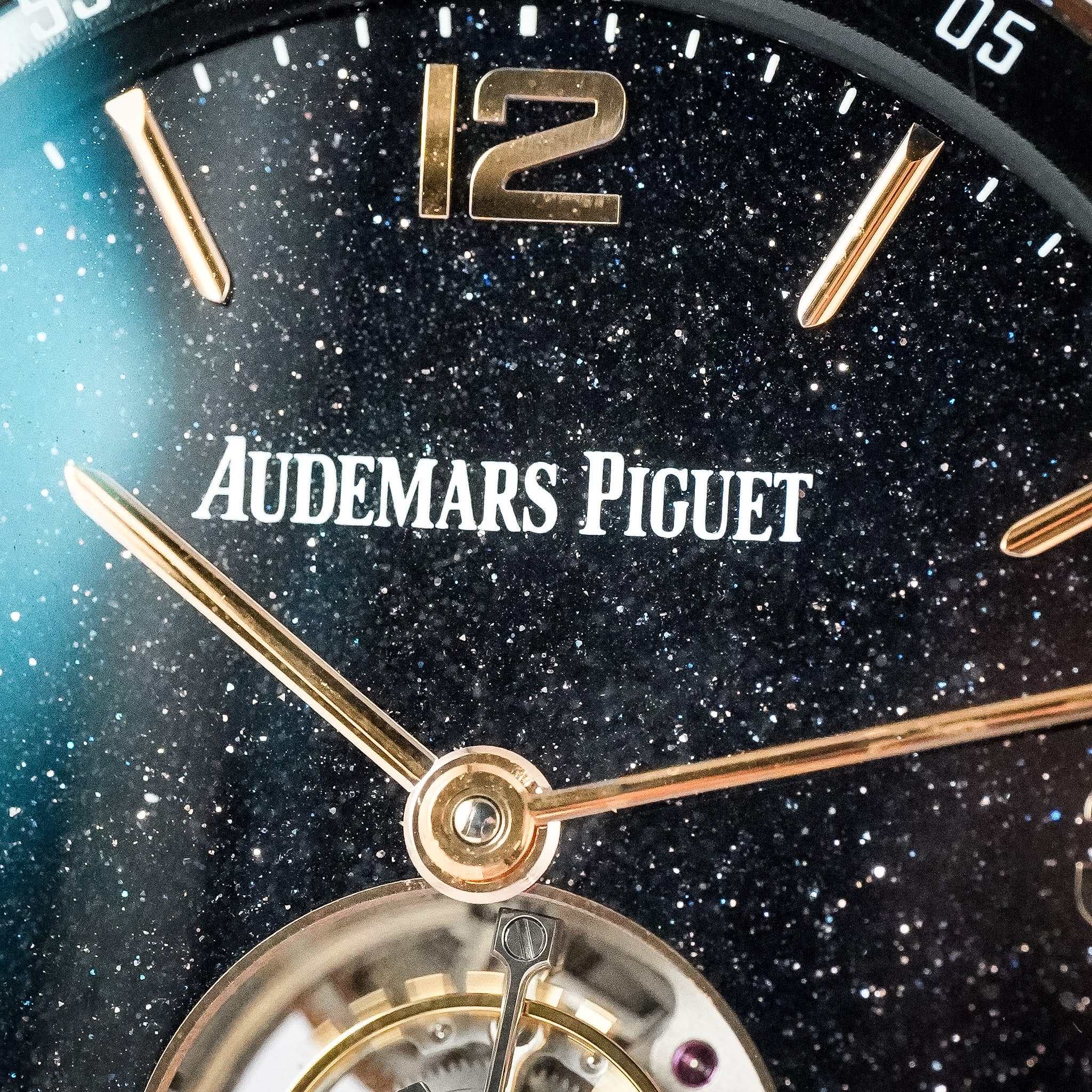 Close-up of an Audemars Piguet watch dial with a black galaxy-style speckled face, gold-tone hands and markers, and the Audemars Piguet logo in white at the 12 o'clock position.
