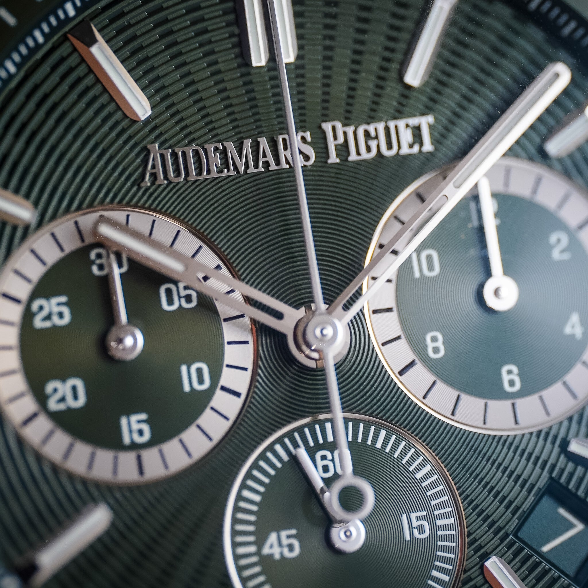 Close-up of an Audemars Piguet watch dial with a dark green textured background, silver-tone hands and markers, and three subdials.