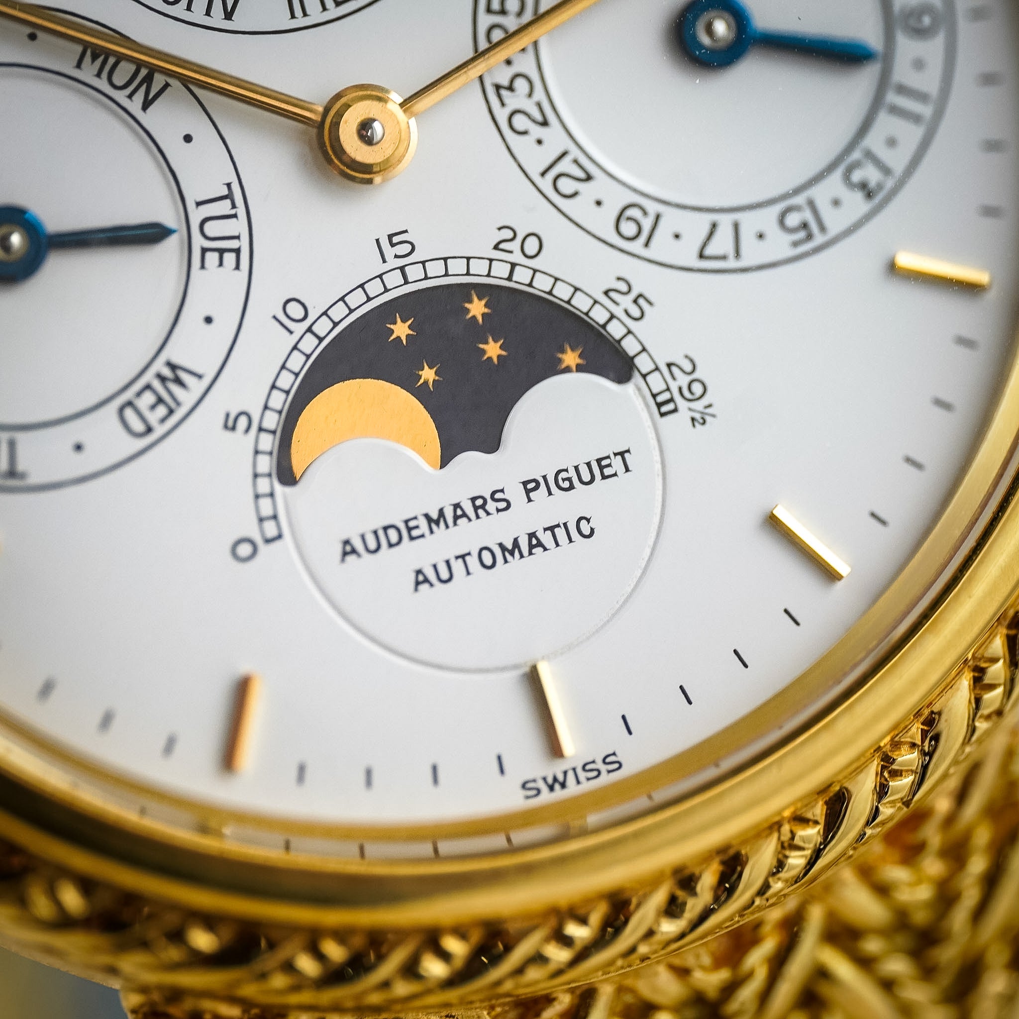 Close-up of an Audemars Piguet Automatic watch dial with a gold case, white subdials, a moon phase indicator, and gold hour markers.