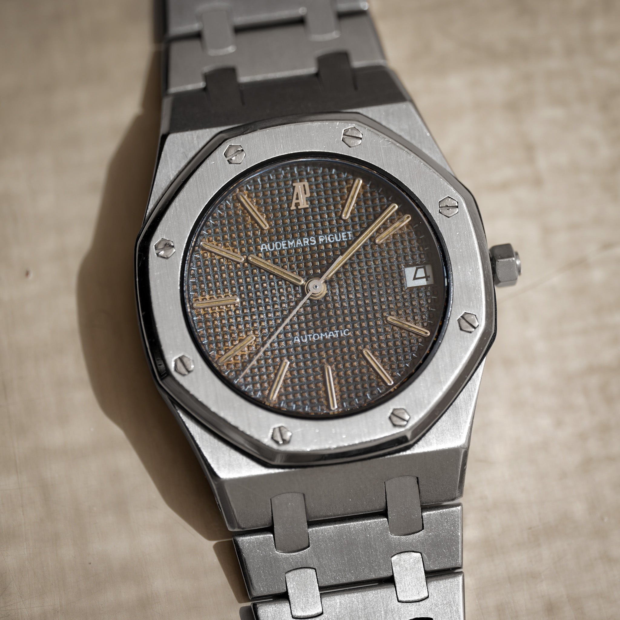 An Audemars Piguet Royal Oak Automatic watch with a silver stainless steel case and bracelet, featuring a textured brown dial with gold-tone indices and hands.