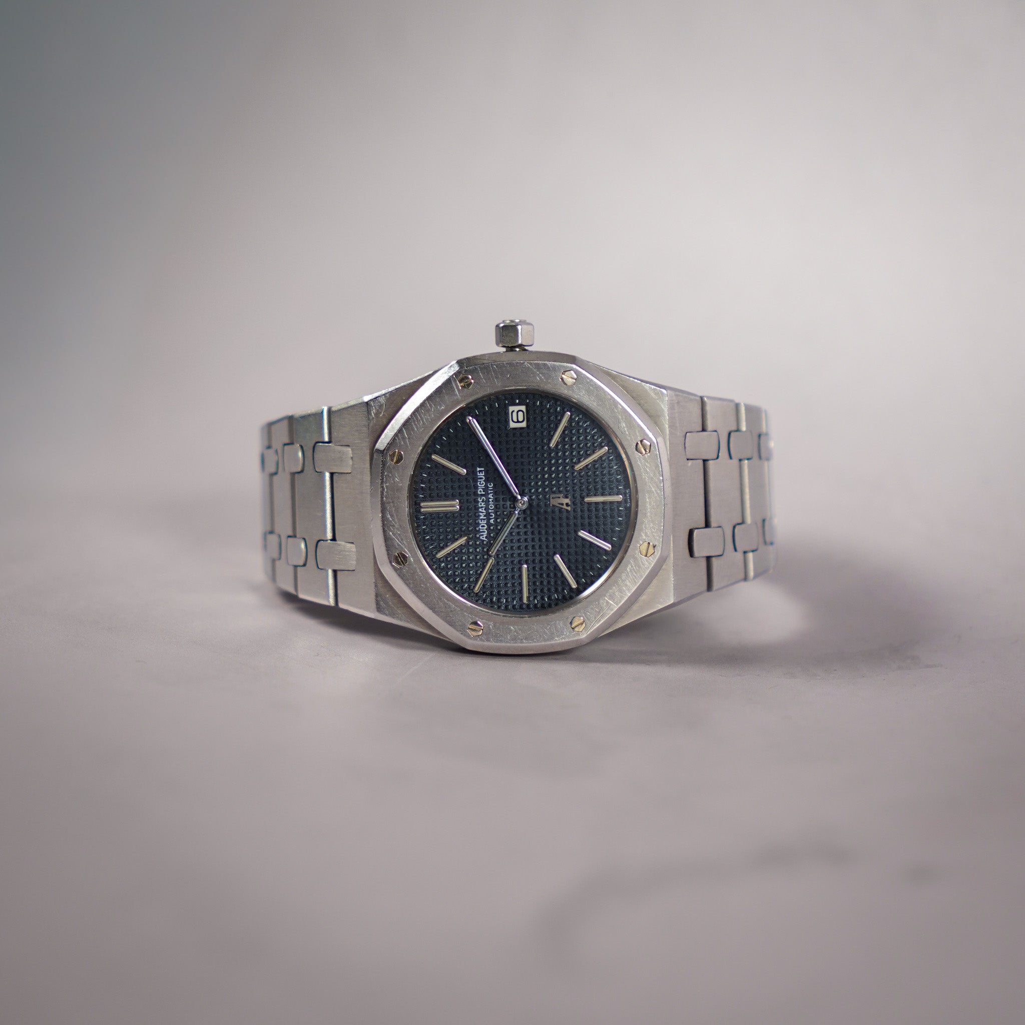 A vintage stainless steel Audemars Piguet Royal Oak watch with a textured blue dial, displayed on a neutral gray background.
