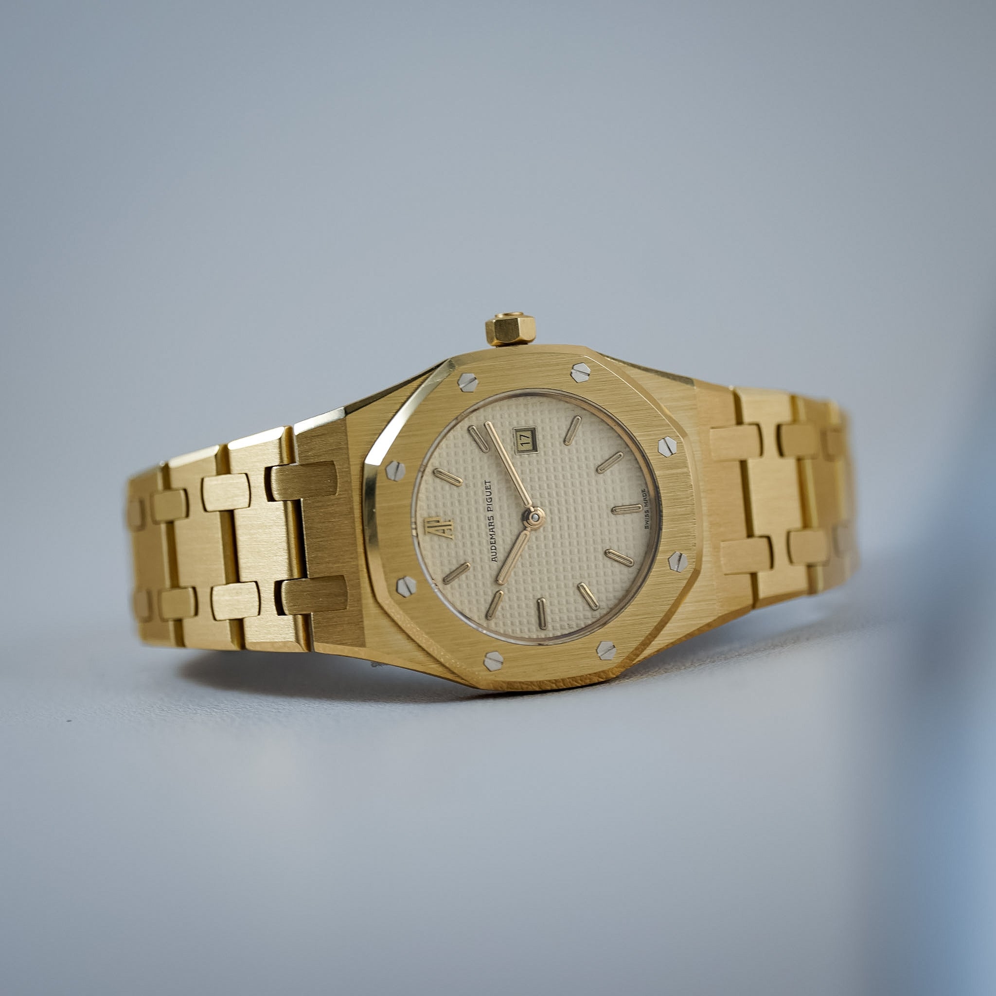 A gold-tone stainless steel wristwatch with an octagonal bezel, date window, and matching link bracelet, photographed on a clean light gray background.