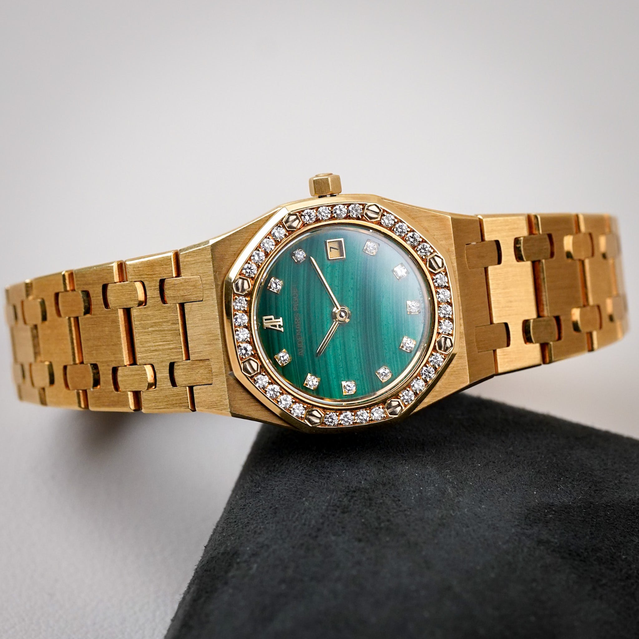 A ladies yellow gold Royak Oak with a malachite dial, diamond bezel and hour markers, and a date window, lying sideways on a black surface with a neutral grey background