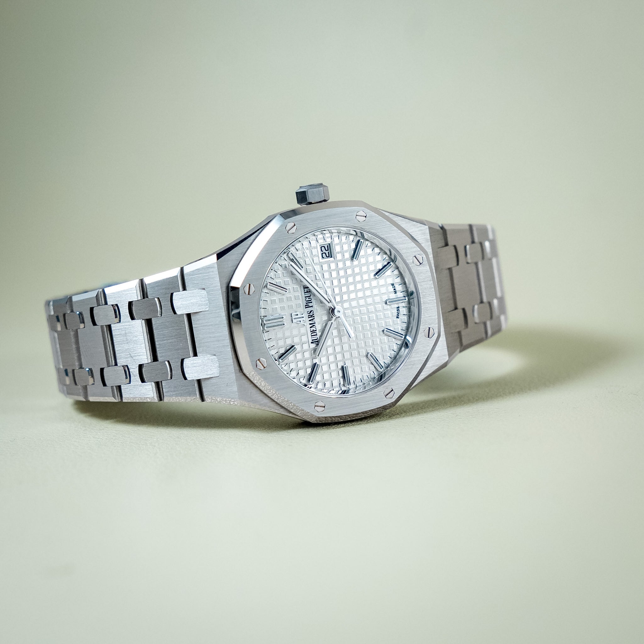 An Audemars Piguet Royal Oak watch with a silver stainless steel octagonal case, textured silver dial, and matching steel bracelet, displayed on a light beige background.